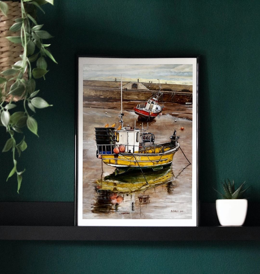 Image of a Large Art Print (A3 size) featuring a copy of the painting 'Lyme Regis at Low Tide' by Nick Dale. As displayed in a frame on a shelf. The print depicts a sunset where the fishing vessels rest on the floor of Lyme Regis harbour whilst the tourists enjoy the view from the Cobb.