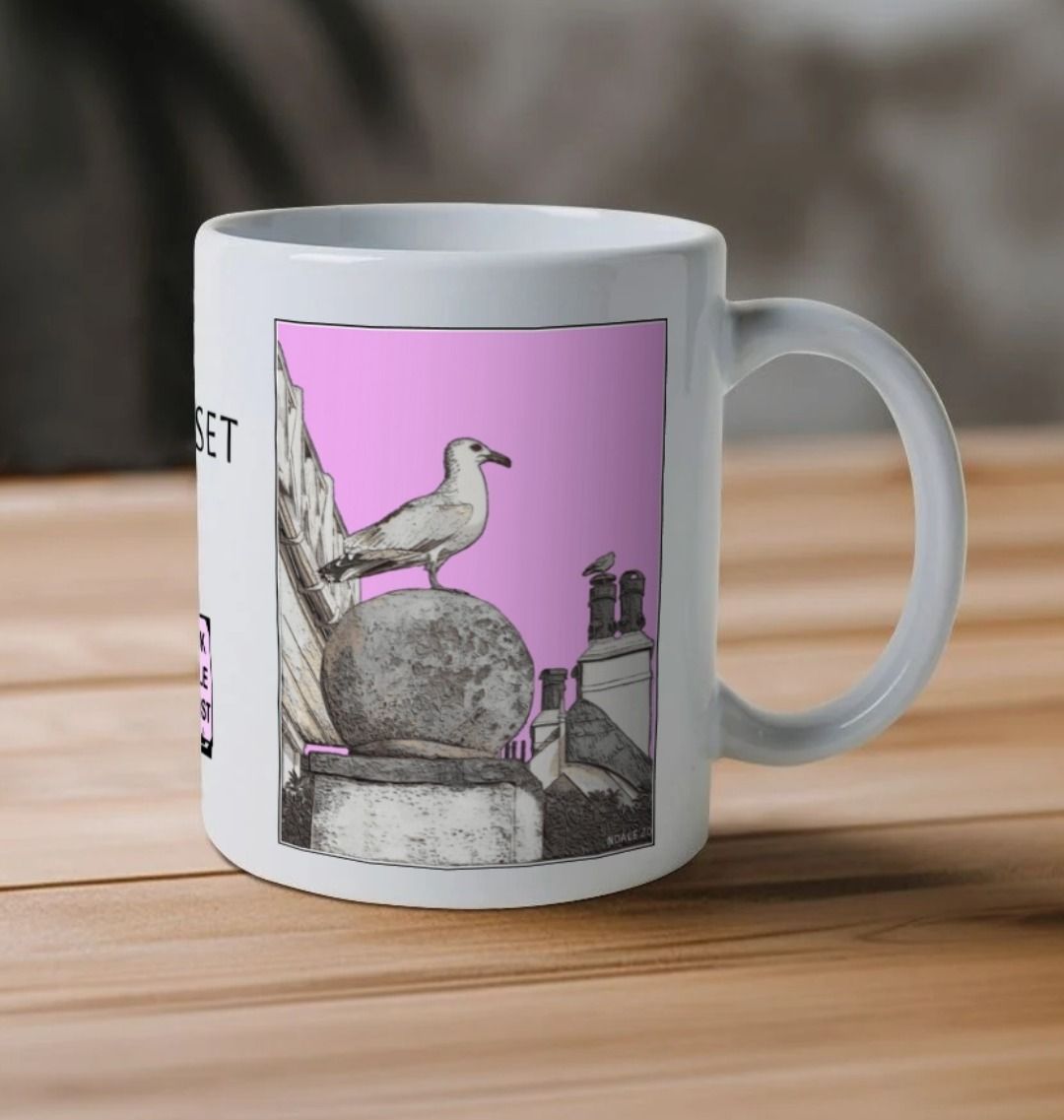 Image of a White Mug on a wooden table featuring a modified copy of the painting 'A View Of The Sea At Lyme Regis' by Nick Dale - this being the 'Pink' version. The handle is orientated to the right. The mug depicts a gull and buildings along Marine Parade, Lyme Regis.