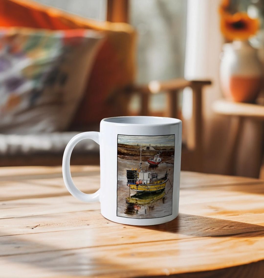 Image of a White Mug on a wooden table featuring a copy of the painting 'Lyme Regis at Low Tide' by Nick Dale. The handle is orientated to the left. The mug depicts a sunset where the fishing vessels rest on the floor of Lyme Regis harbour whilst the tourists enjoy the view from the Cobb.