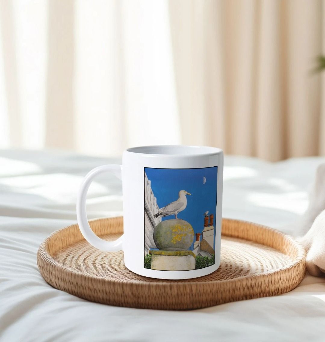 Image of a White Mug on a tray on a bed featuring a copy of the painting 'A View Of The Sea At Lyme Regis' by Nick Dale. The handle is orientated to the left. The mug depicts a gull and buildings along Marine Parade, Lyme Regis.