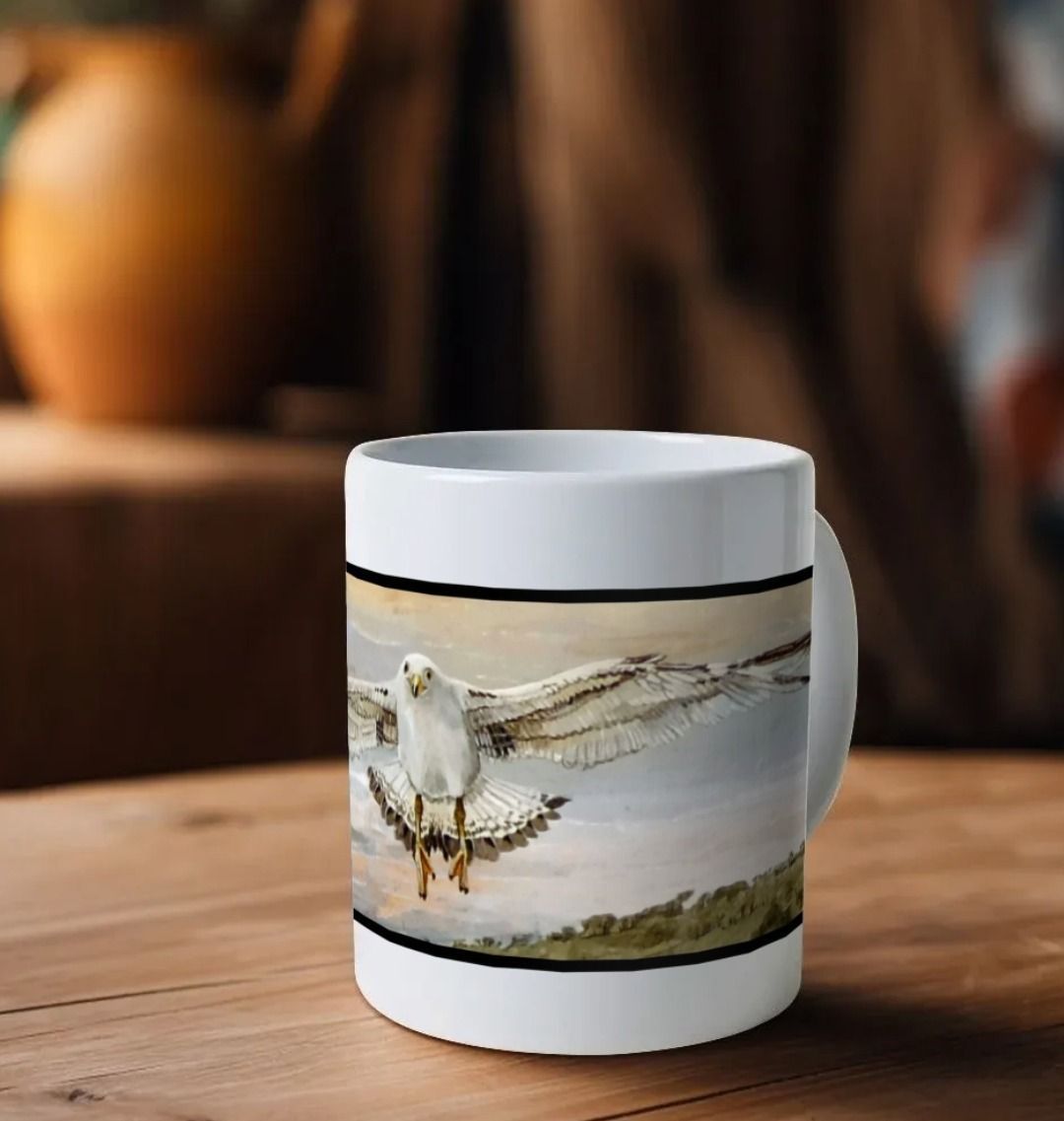 Image of a White Mug on a wooden table featuring a copy of a detail from the painting 'The Gordian Knot At Lyme Regis' by Nick Dale. The mug handle is obscured behind the mug. The mug depicts a gull flying over the Cobb at Lyme Regis, Dorset. The title refers to the jumbled pile of fishing equipment sitting on the quayside visible in the original painting.