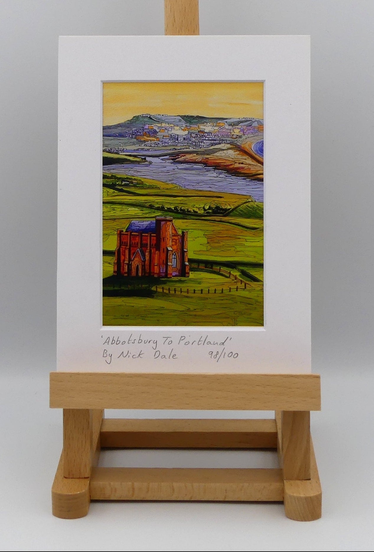 Image of a Small Art Print featuring a copy of the painting 'Abbotsbury To Portland' by Nick Dale. The print depicts the view along the Dorset coast from St Catherine's Chapel above Abbotsbury, across The Fleet lagoon to Chesil Beach and ultimately to Portland beyond it. The print is situated on a small easel.