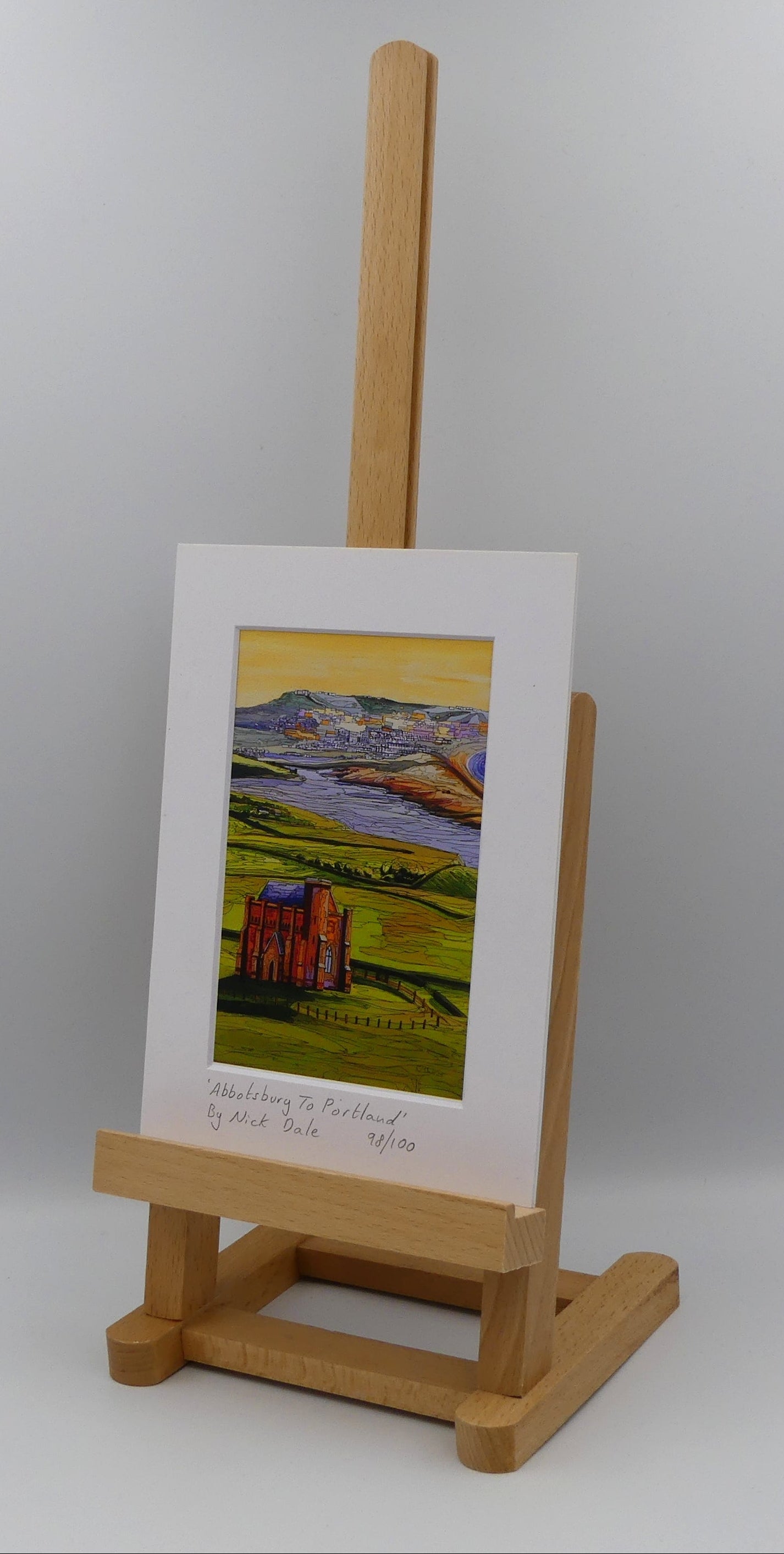 Image of a Small Art Print featuring a copy of the painting 'Abbotsbury To Portland' by Nick Dale. The print depicts the view along the Dorset coast from St Catherine's Chapel above Abbotsbury, across The Fleet lagoon to Chesil Beach and ultimately to Portland beyond it. The print is situated on a small easel.