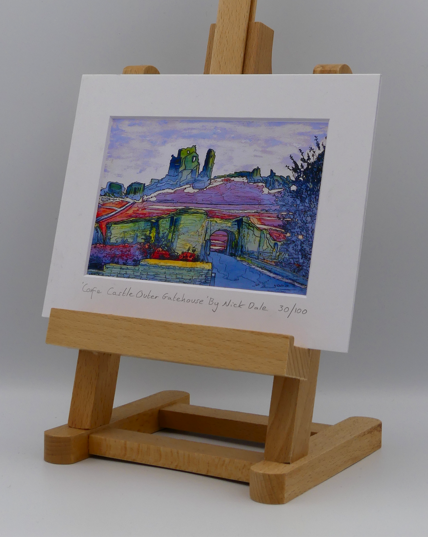 Image of a Small Art Print featuring a copy of the painting 'Corfe Castle Outer Gatehouse' by Nick Dale. The print depicts the slighted outer gatehouse of Corfe Castle in the village of Corfe Castle, Dorset. Beyond it can be seen the castle's south-west gatehouse and keep on top of the central hilltop. The print is situated on a small easel.