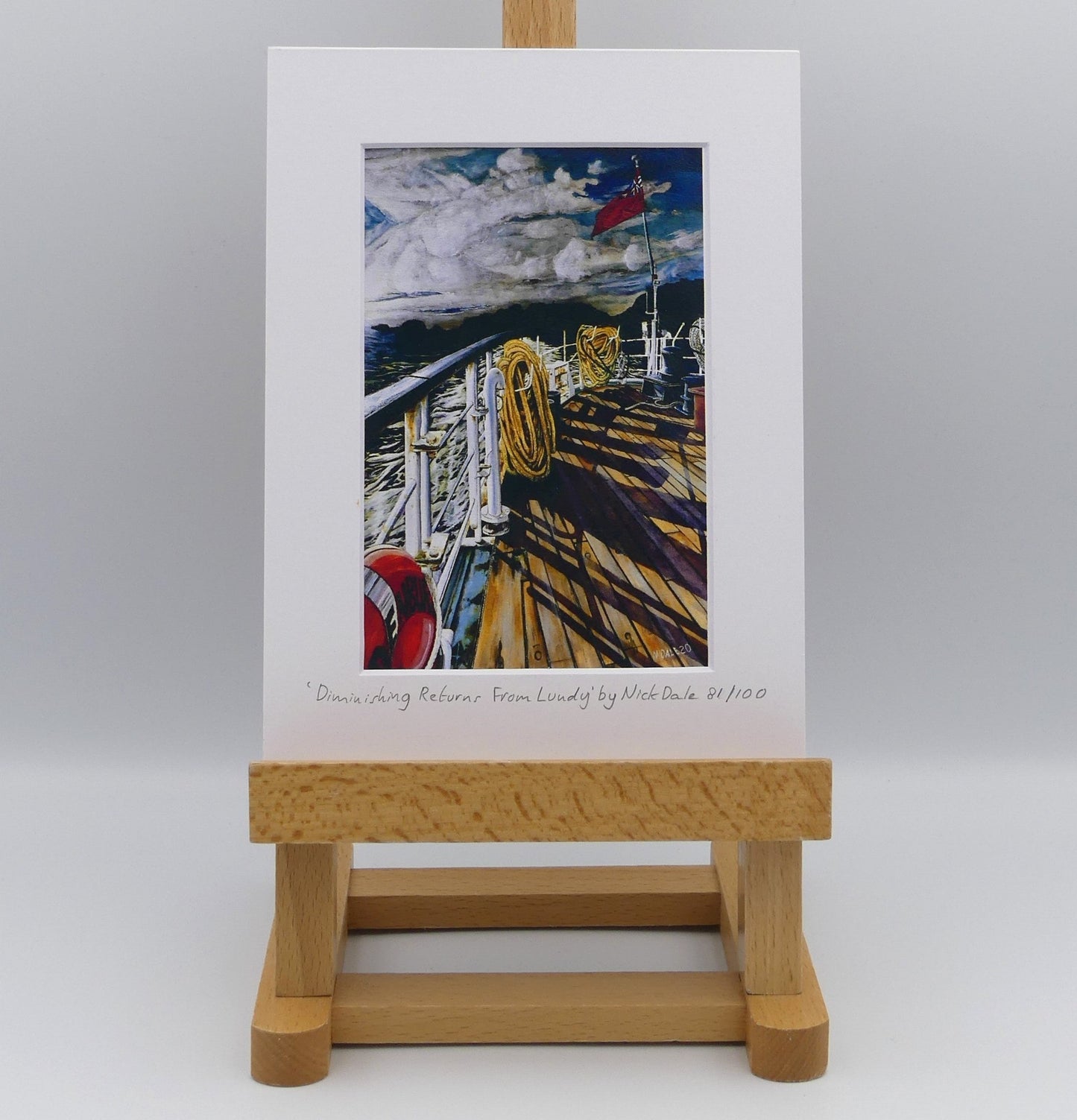 Image of Small Art Print featuring a copy of the painting 'Diminishing Returns From Lundy' by Nick Dale. The print depicts the stern of the ship MS Oldenburg as it returns to the mainland from Lundy Island, Devon. As the sun goes down it casts long shadows on the deck. whilst the flag flutters in the breeze. The Silhouette of the island can be seen diminishing into the background. The print is situated on a small easel.
