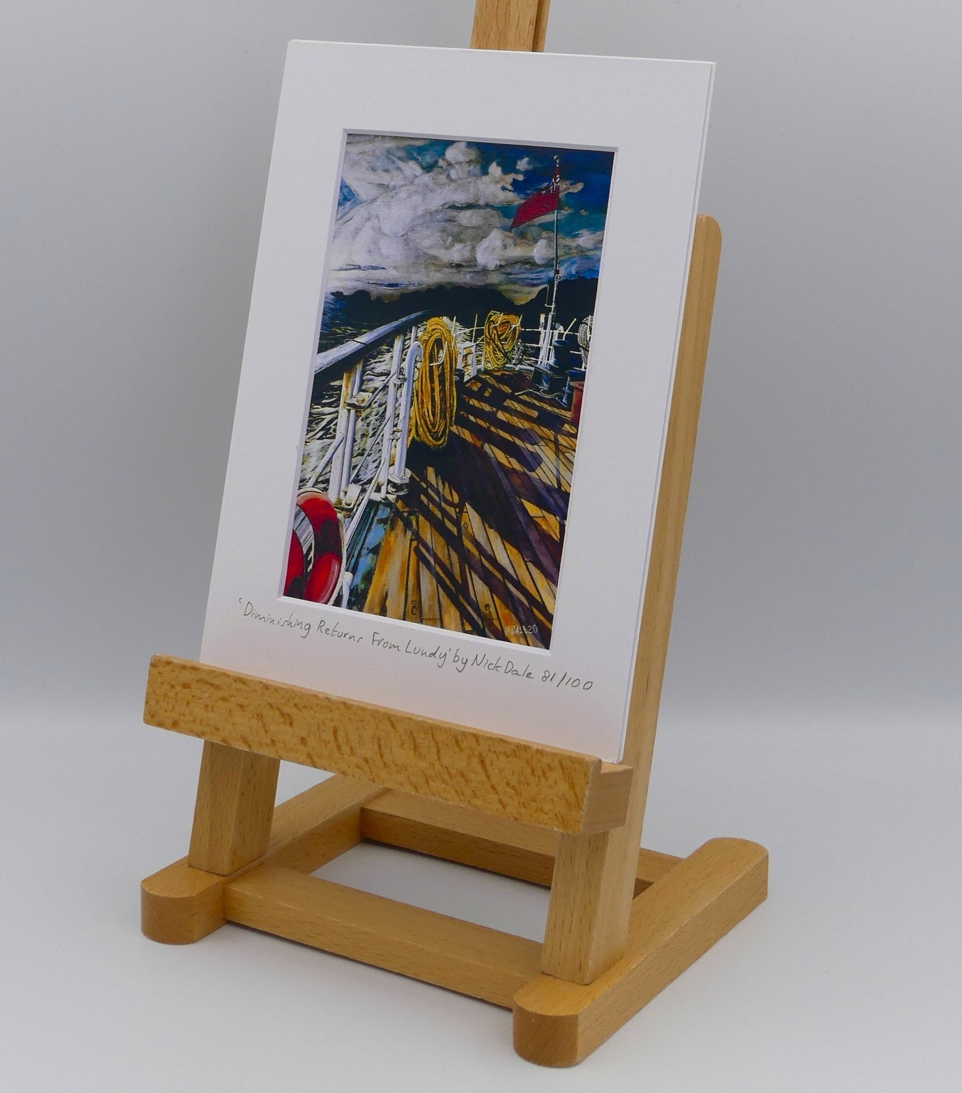 Image of Small Art Print featuring a copy of the painting 'Diminishing Returns From Lundy' by Nick Dale. The print depicts the stern of the ship MS Oldenburg as it returns to the mainland from Lundy Island, Devon. As the sun goes down it casts long shadows on the deck. whilst the flag flutters in the breeze. The Silhouette of the island can be seen diminishing into the background. The print is situated on a small easel.