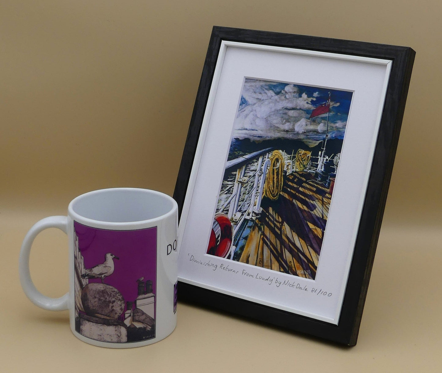 Image of Small Art Print featuring a copy of the painting 'Diminishing Returns From Lundy' by Nick Dale. The print depicts the stern of the ship MS Oldenburg as it returns to the mainland from Lundy Island, Devon. As the sun goes down it casts long shadows on the deck. whilst the flag flutters in the breeze. The Silhouette of the island can be seen diminishing into the background. The print is situated in a black frame next to a mug.