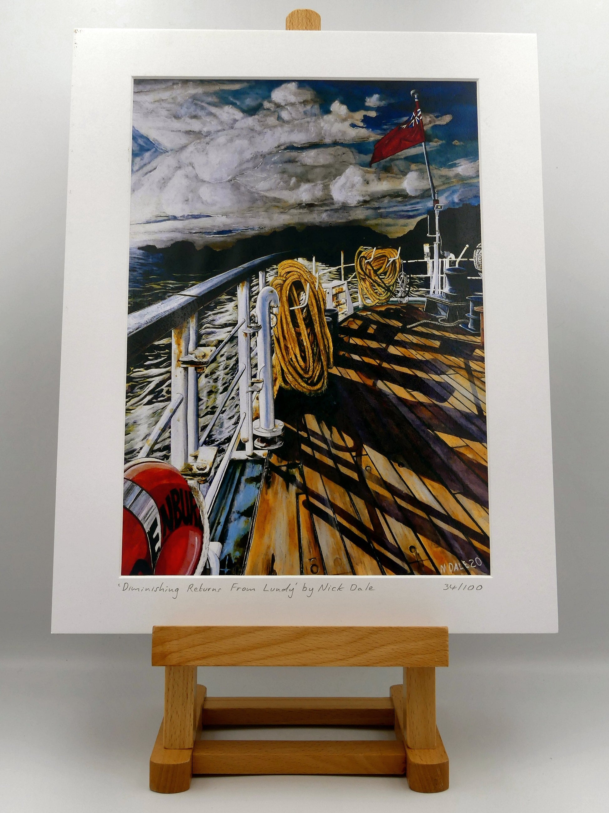 Image of Medium Art Print featuring a copy of the painting 'Diminishing Returns From Lundy' by Nick Dale. The print depicts the stern of the ship MS Oldenburg as it returns to the mainland from Lundy Island, Devon. As the sun goes down it casts long shadows on the deck. whilst the flag flutters in the breeze. The Silhouette of the island can be seen diminishing into the background. The print is situated on a small easel.