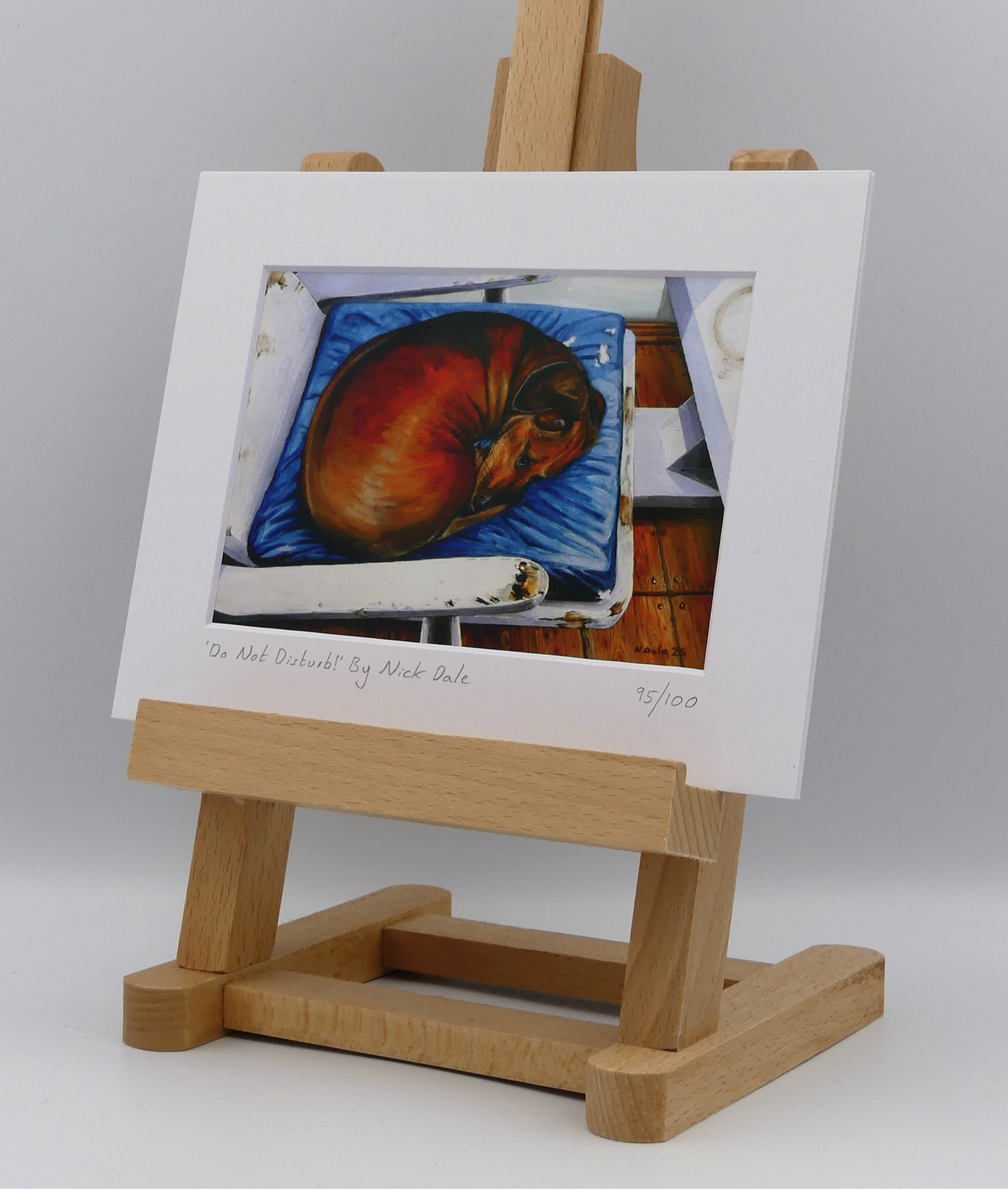 Image of a Small Art Print featuring a copy of the painting 'Do Not Disturb' by Nick Dale. The print depicts a miniature dachshund dog curled up on a favourite seat. Its gaze clearly indicates that it is not keen on being evicted from its current location and slumbering state. The print is situated on a small easel.