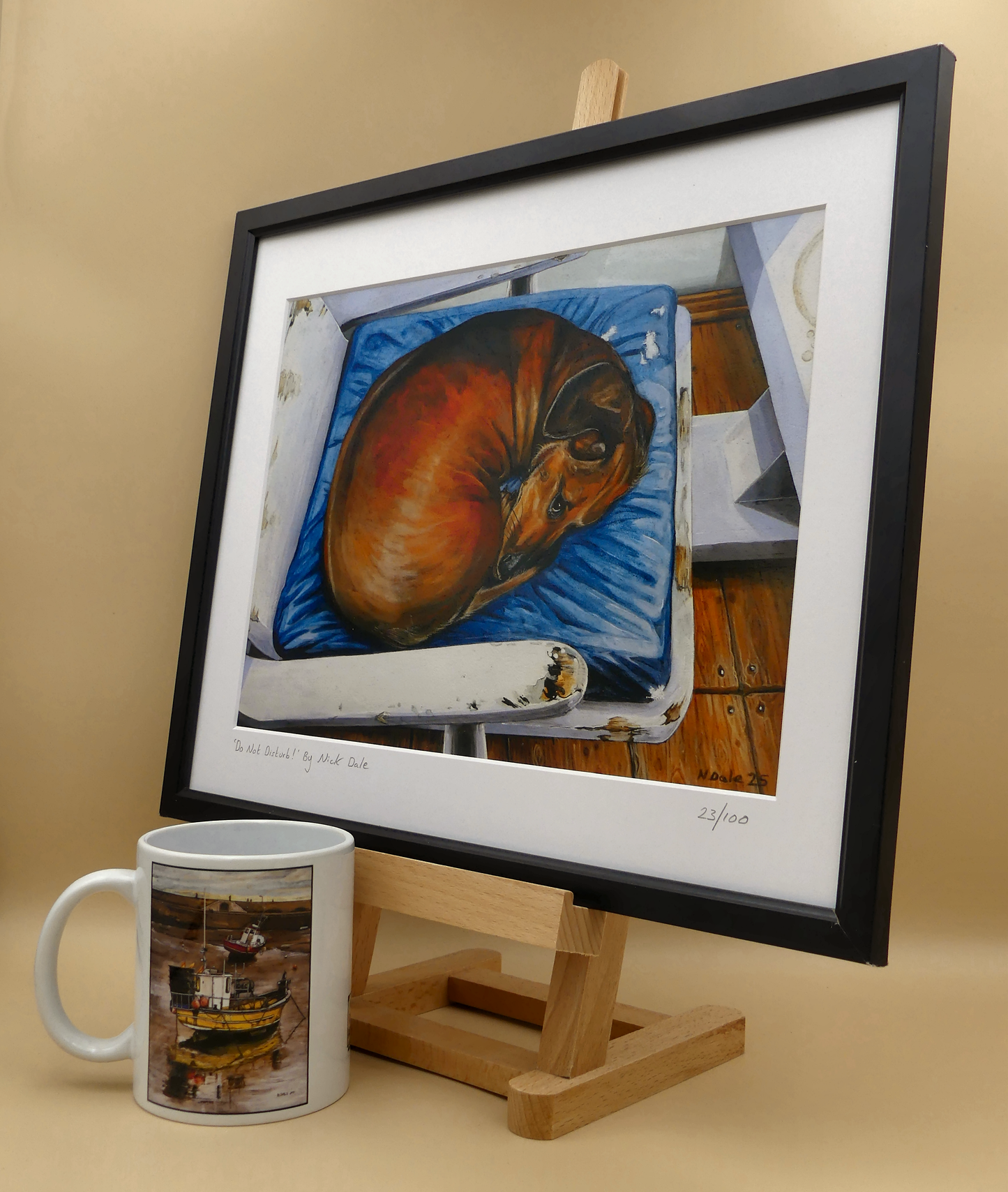 Image of a Medium Art Print featuring a copy of the painting 'Do Not Disturb' by Nick Dale. depicts a miniature dachshund dog curled up on a favourite seat. Its gaze clearly indicates that it is not keen on being evicted from its current location and slumbering state. The print is situated on a small easel in a black frame next to a mug.