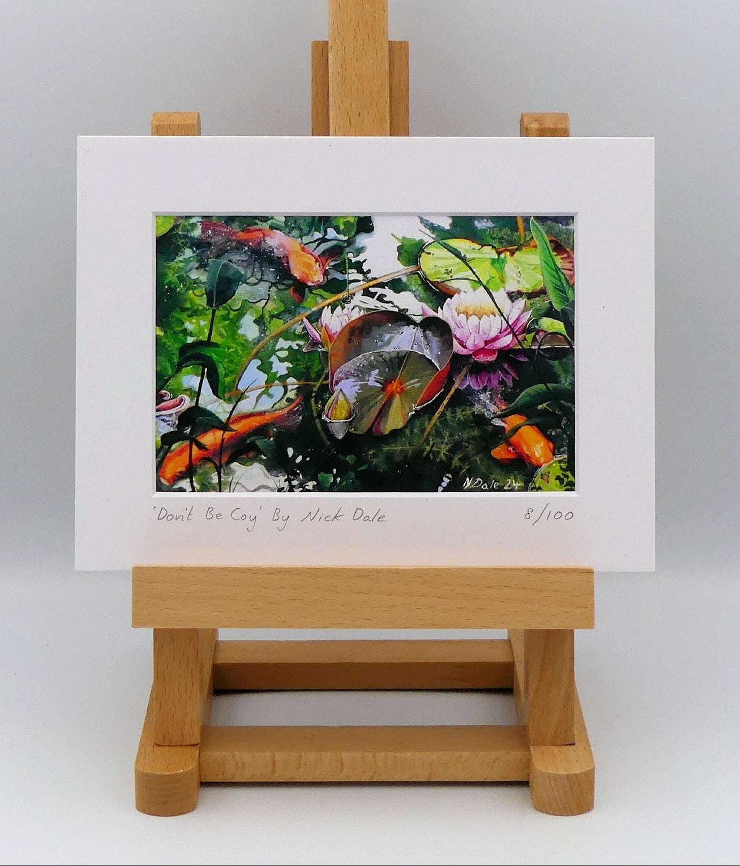 Image of a Small Art Print featuring a copy of the painting 'Don't Be Coy' by Nick Dale. The print depicts 3 koi carp along with water lilies and their flowers. The painting is based on fish and lilies observed at Bennetts Water Gardens in Weymouth, Dorset. The title is a play on the homophones 'Coy' and 'Koi'.  The print is situated on a small easel.