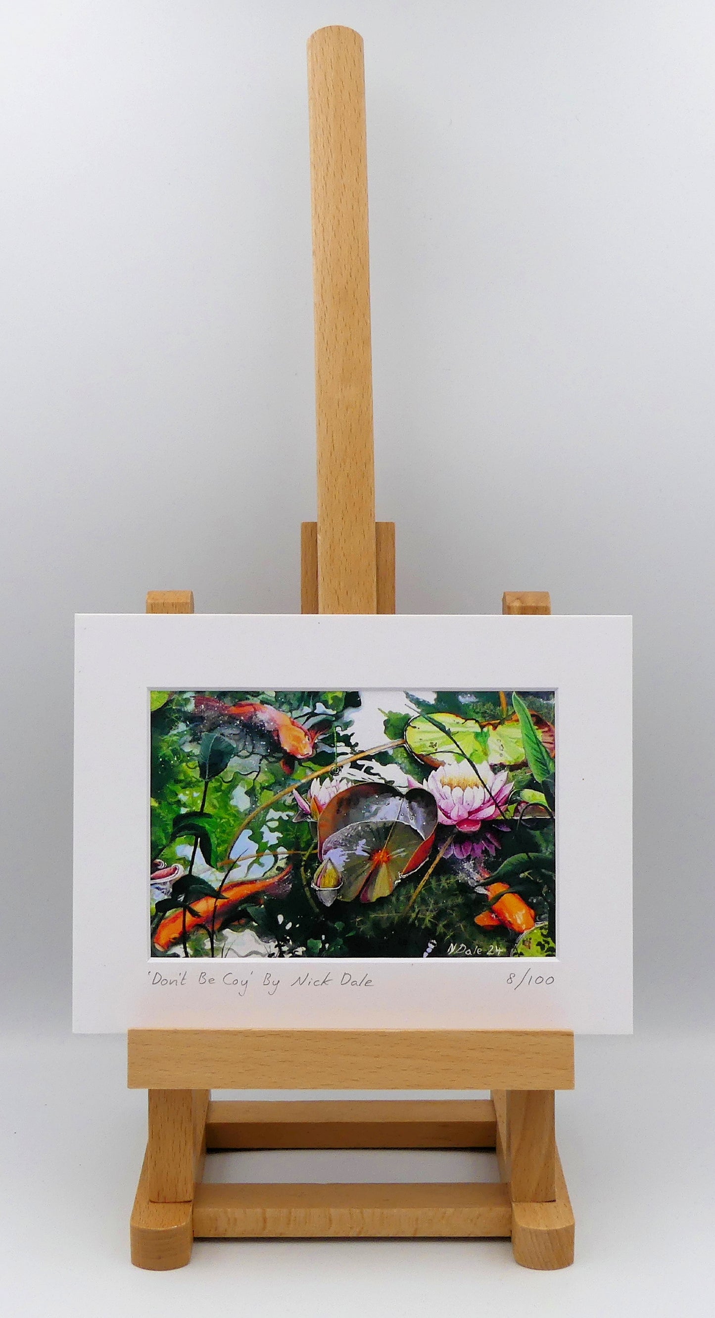 Image of a Small Art Print featuring a copy of the painting 'Don't Be Coy' by Nick Dale. The print depicts 3 koi carp along with water lilies and their flowers. The painting is based on fish and lilies observed at Bennetts Water Gardens in Weymouth, Dorset. The title is a play on the homophones 'Coy' and 'Koi'. The print is situated on a small easel.