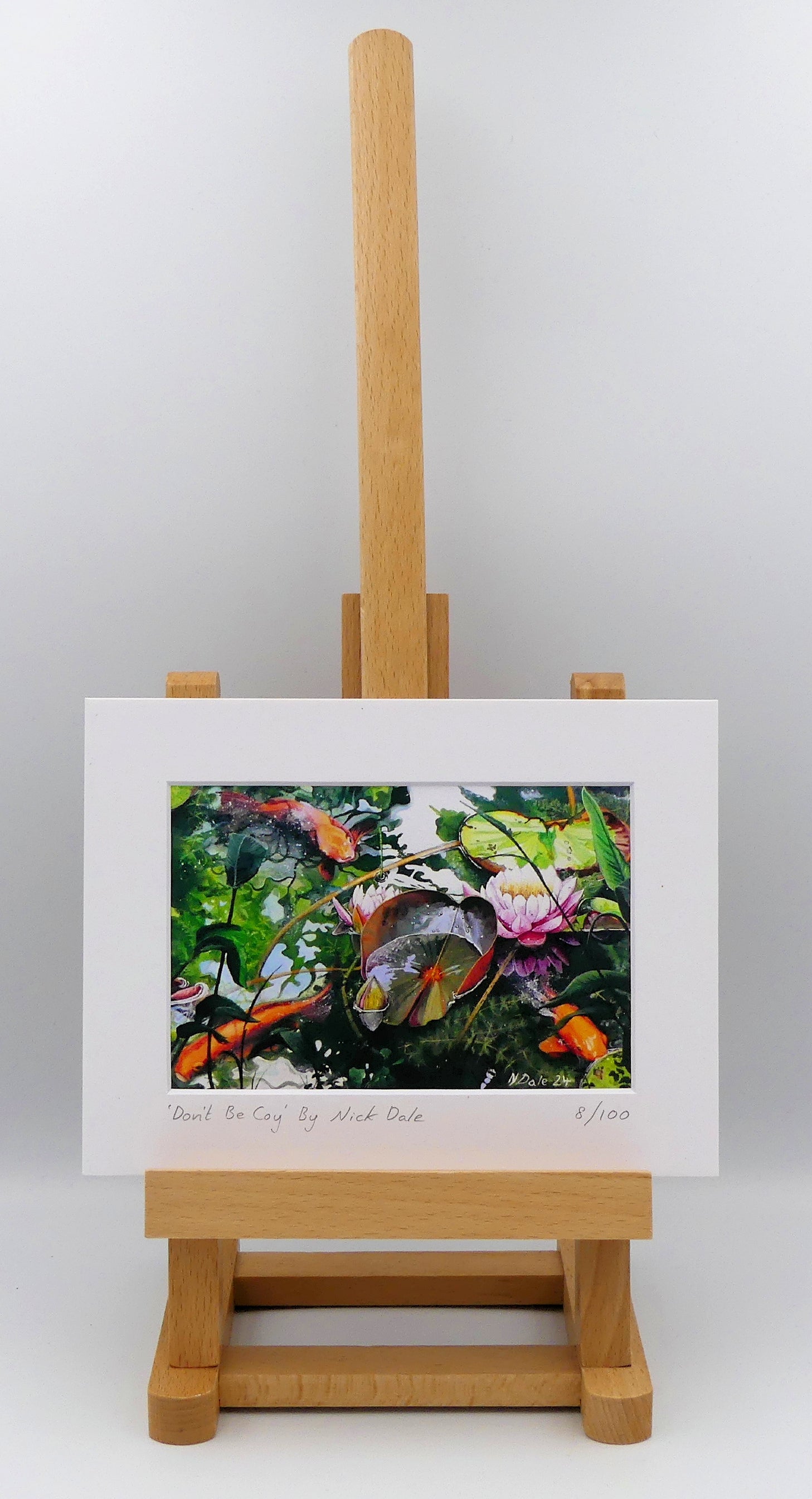 Image of a Small Art Print featuring a copy of the painting 'Don't Be Coy' by Nick Dale. The print depicts 3 koi carp along with water lilies and their flowers. The painting is based on fish and lilies observed at Bennetts Water Gardens in Weymouth, Dorset. The title is a play on the homophones 'Coy' and 'Koi'. The print is situated on a small easel.
