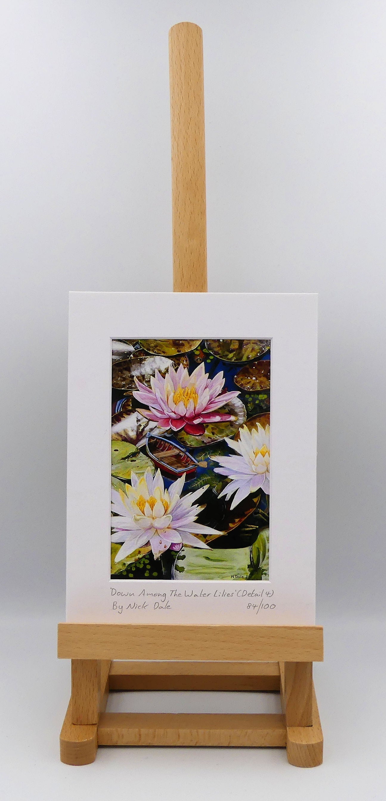 Image of a Small Art Print featuring a copy of a detail from the painting 'Down Among The Water Lilies' by Nick Dale. The print depicts the part of the original painting showing the rowing boat and a close-up view of the water lilies at Bennetts Water Gardens in Weymouth, with the twist of the boat being shrunk down to lilliputian dimensions. The print is situated on a small easel.