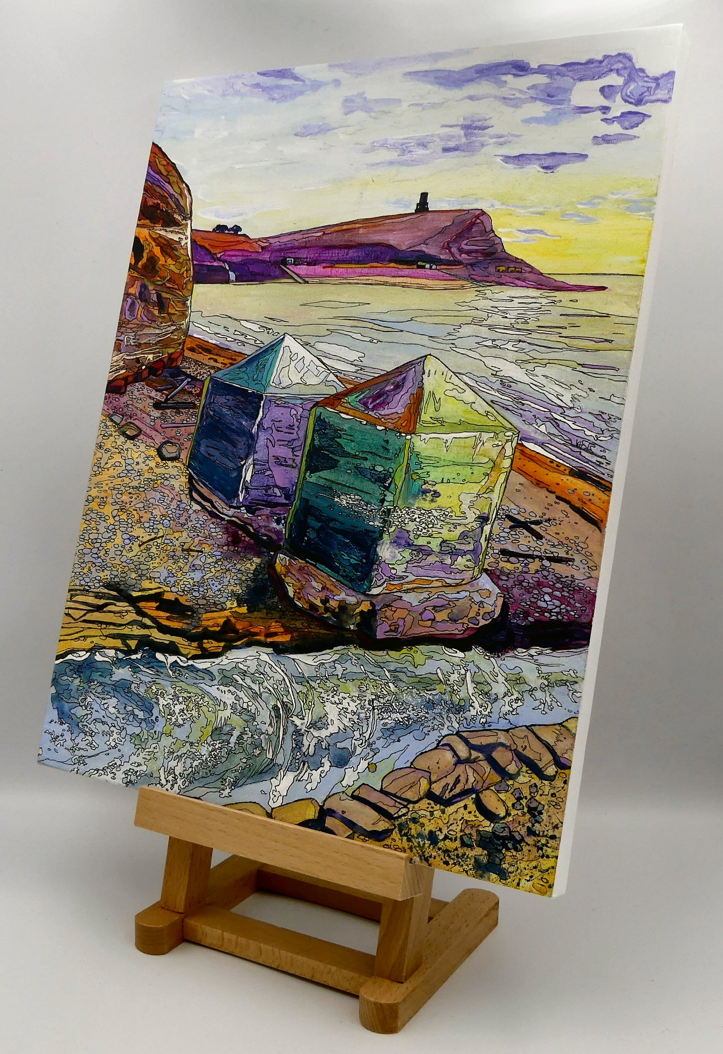 Image of the original painting 'Dragon's Teeth, Kimmeridge' by Nick Dale on an easel. The scene depicts two surviving dragon's teeth anti-tank defences on the beach at Kimmeridge Bay, Dorset. Beyond them can be seen Clavell Tower on the cliff top.
The Gaulter Gap forms a relatively easy route off the beach to the cliffs above for any invading force so it was blocked with dragon's teeth and a concrete pillbox during World War II.
