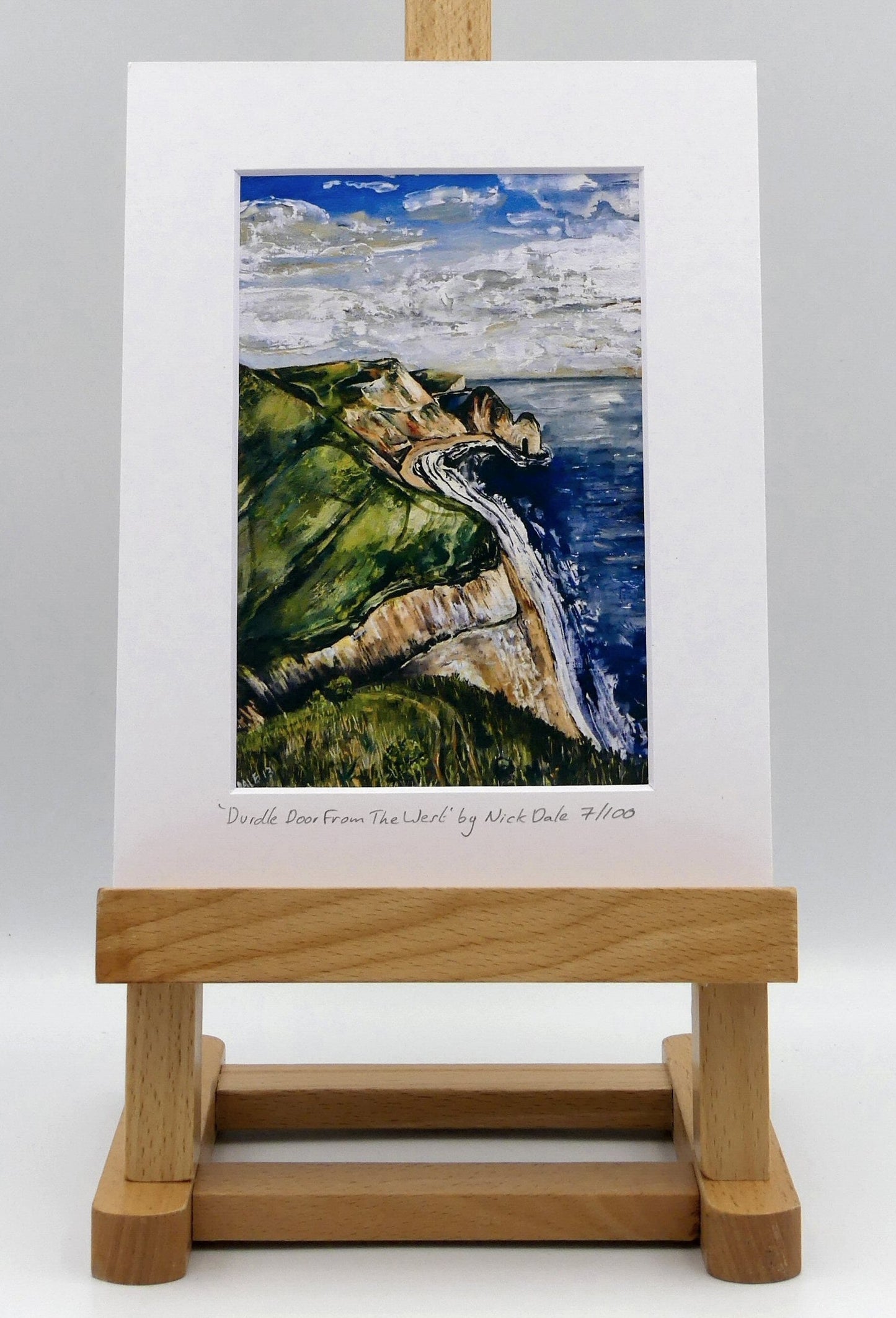 Image of a Small Art Print featuring a copy of the painting 'Durdle Door From The West:' by Nick Dale. The print depicts a view along the Jurassic Coast to the famous Dorset limestone arch landmark, as seen from the coastal path to the west. The print is situated on a small easel.
