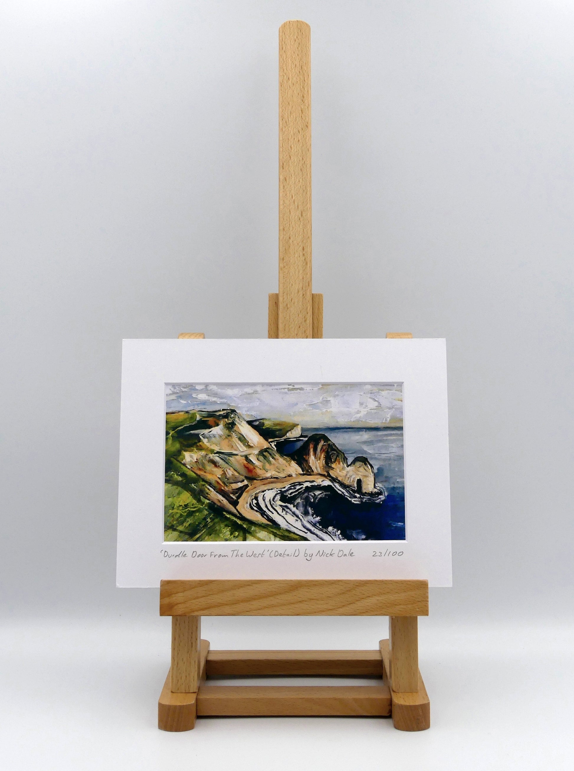 Image of a Small Art Print featuring a copy of a detail from the painting 'Durdle Door From The West:' by Nick Dale. The print depicts a view along the Jurassic Coast to the famous Dorset limestone arch landmark, as seen from the coastal path to the west. The print is situated on a small easel.