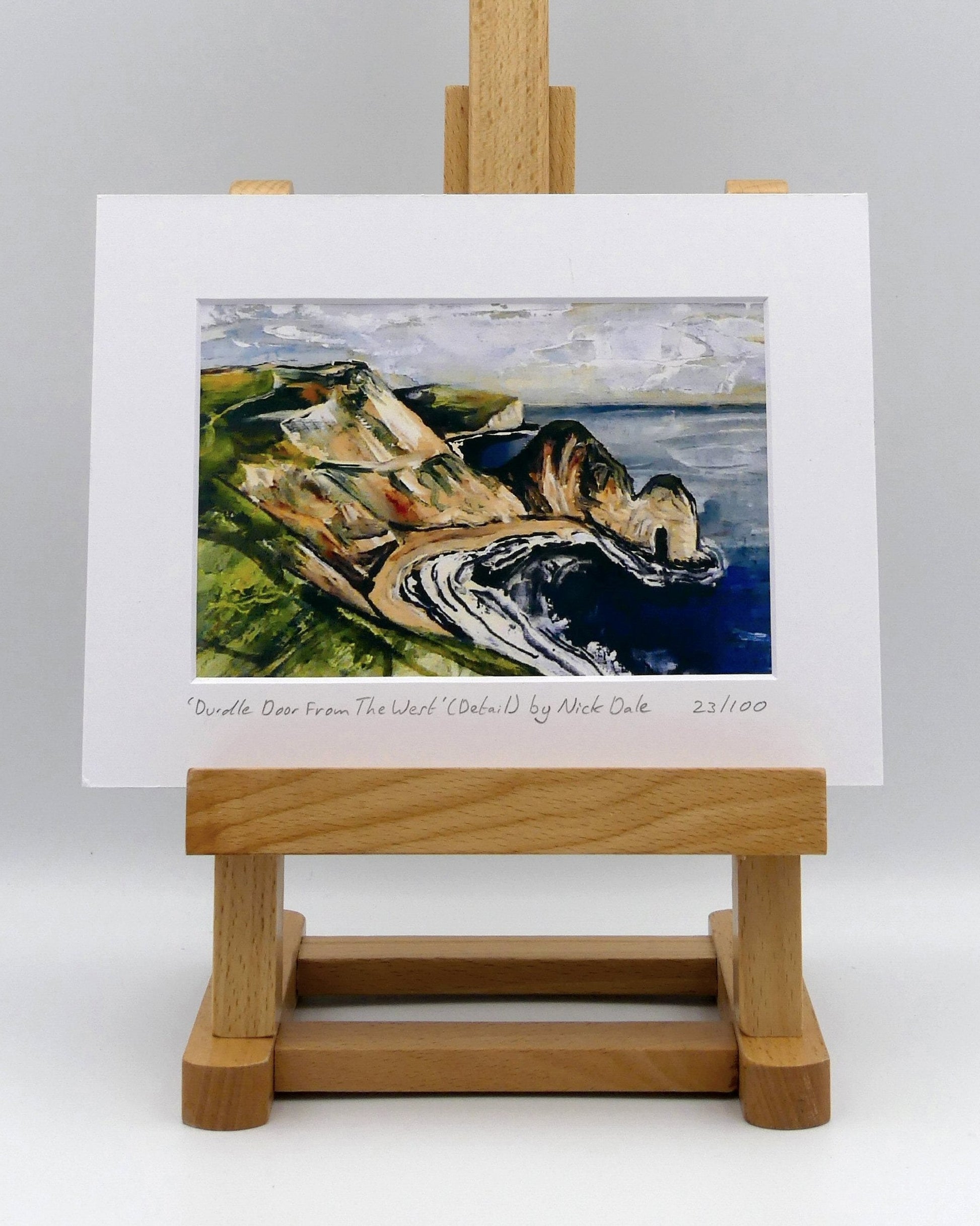 Image of a Small Art Print featuring a copy of a detail from the painting 'Durdle Door From The West:' by Nick Dale. The print depicts a view along the Jurassic Coast to the famous Dorset limestone arch landmark, as seen from the coastal path to the west. The print is situated on a small easel.