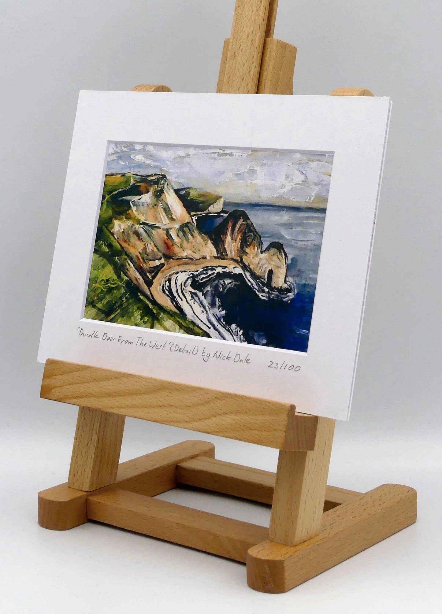 Image of a Small Art Print featuring a copy of a detail from the painting 'Durdle Door From The West:' by Nick Dale. The print depicts a view along the Jurassic Coast to the famous Dorset limestone arch landmark, as seen from the coastal path to the west. The print is situated on a small easel.