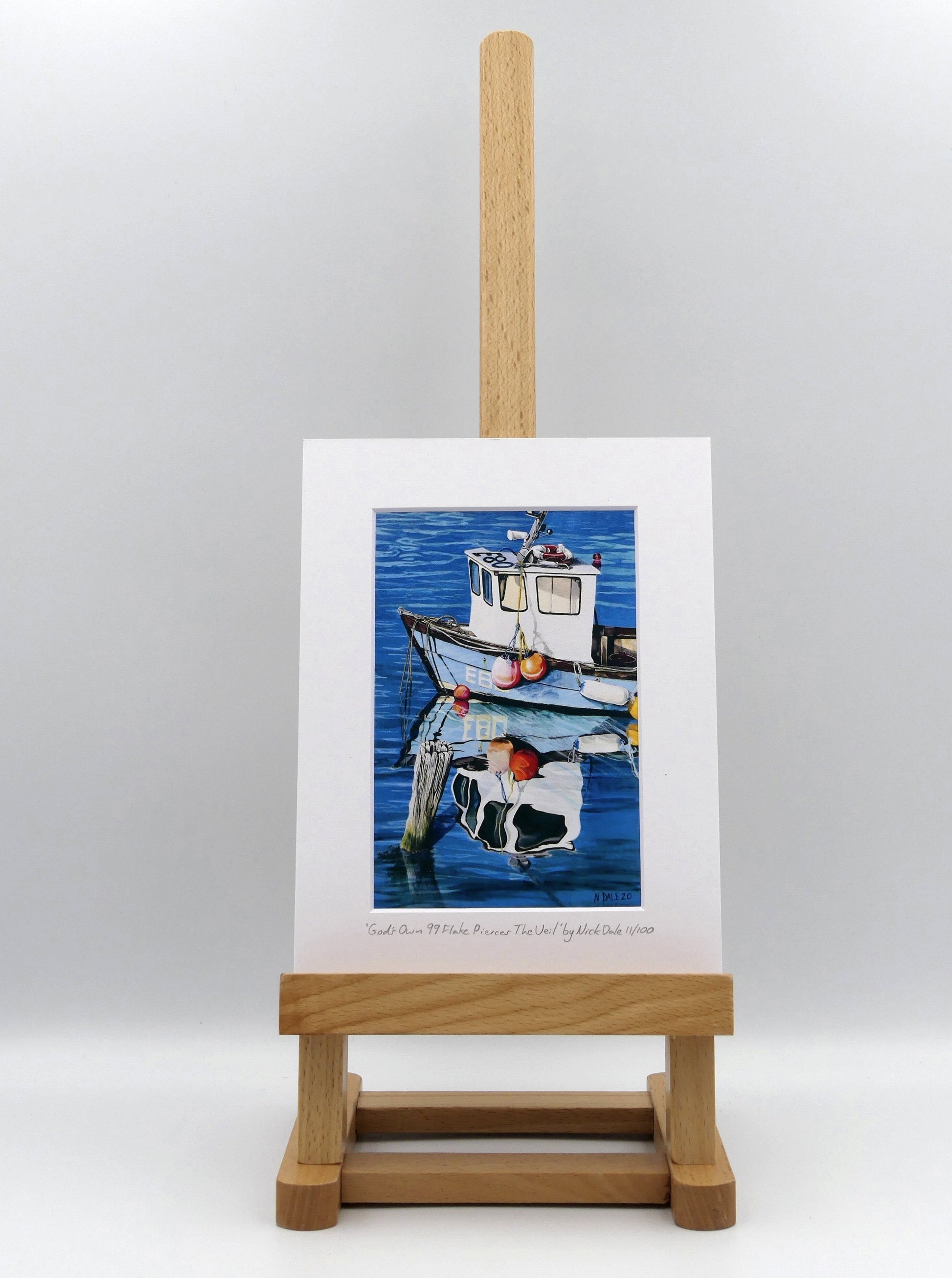 Image of a Small Art Print featuring a copy of the painting 'God's Own 99 Flake Pierces The Veil' by Nick Dale. The print depicts a fishing boat at rest within the harbour of Lyme Regis, Dorset. The title is based on the similarity of the wooden pile to a chocolate flake as inserted into an ice cream cone. This seemed appropriate given the draw of the town to tourists. The print is situated on a small easel.