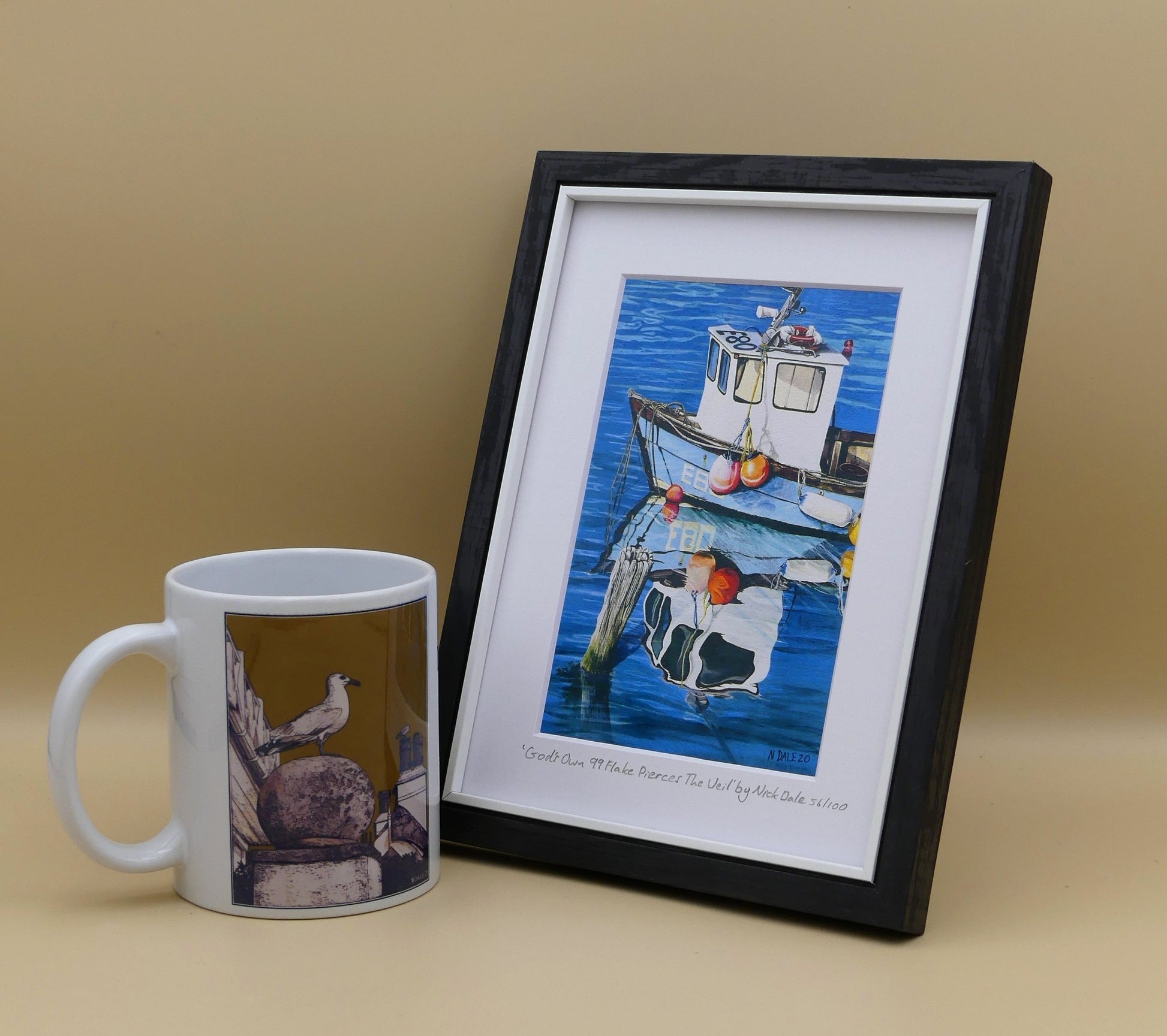 Image of a Small Art Print featuring a copy of the painting 'God's Own 99 Flake Pierces The Veil' by Nick Dale. The print depicts a fishing boat at rest within the harbour of Lyme Regis, Dorset. The title is based on the similarity of the wooden pile to a chocolate flake as inserted into an ice cream cone. This seemed appropriate given the draw of the town to tourists. The print is situated in a black frame next to a mug.