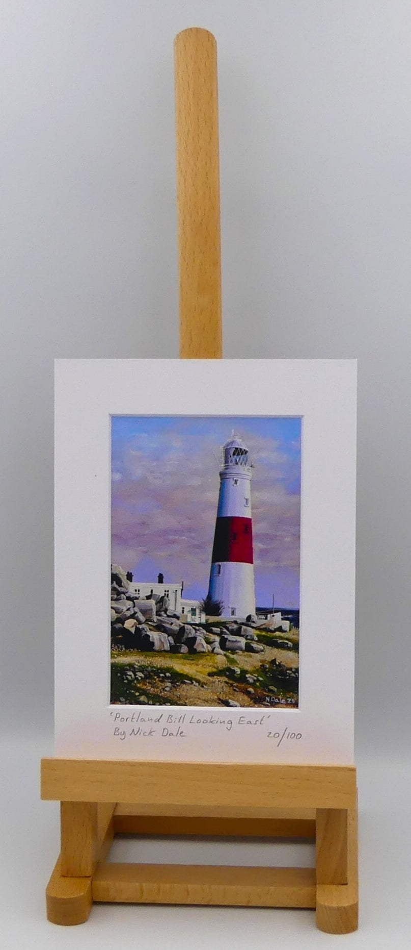 Image of a Small Art Print featuring a copy of the painting 'Portland Bill Looking East' by Nick Dale. The print depicts a view of Portland Bill Lighthouse as seen from the quarry area to the west, looking east. The print is situated on a small easel.