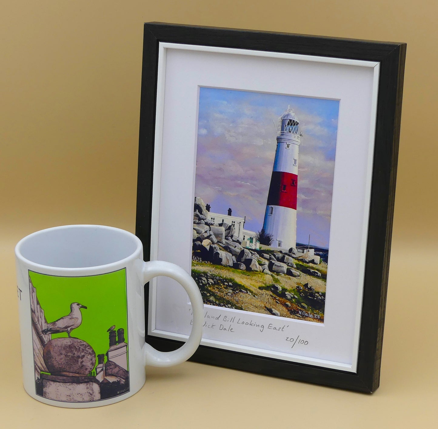 Image of a Small Art Print featuring a copy of the painting 'Portland Bill Looking East' by Nick Dale. The print depicts a view of Portland Bill Lighthouse as seen from the quarry area to the west, looking east. The print is situated in a black frame next to a mug.
