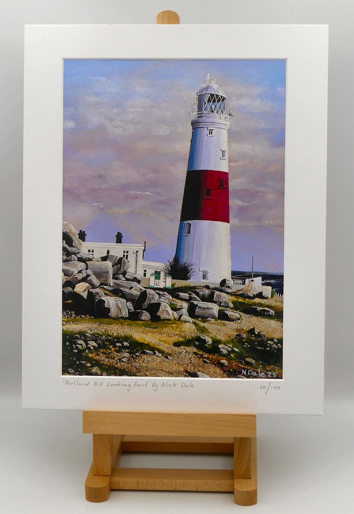 Image of a Medium Art Print featuring a copy of the painting 'Portland Bill Looking East' by Nick Dale. The print depicts a view of Portland Bill Lighthouse as seen from the quarry area to the west, looking east. The print is situated on a small easel.