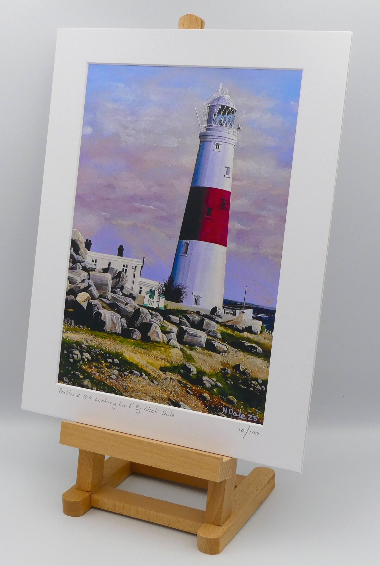 Image of a Medium Art Print featuring a copy of the painting 'Portland Bill Looking East' by Nick Dale. The print depicts a view of Portland Bill Lighthouse as seen from the quarry area to the west, looking east. The print is situated on a small easel.