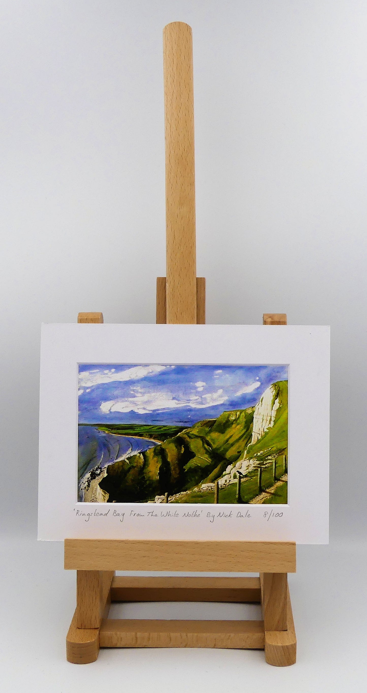 Image of a Small Art Print featuring a copy of the painting 'Ringstead Bay From The White Nothe' by Nick Dale. The print depicts a view along the Jurassic Coast from the White Nothe chalk headland east of Ringstead Bay. The view looks west over the bay to the village of Ringstead & beyond. The print is situated on a small easel.