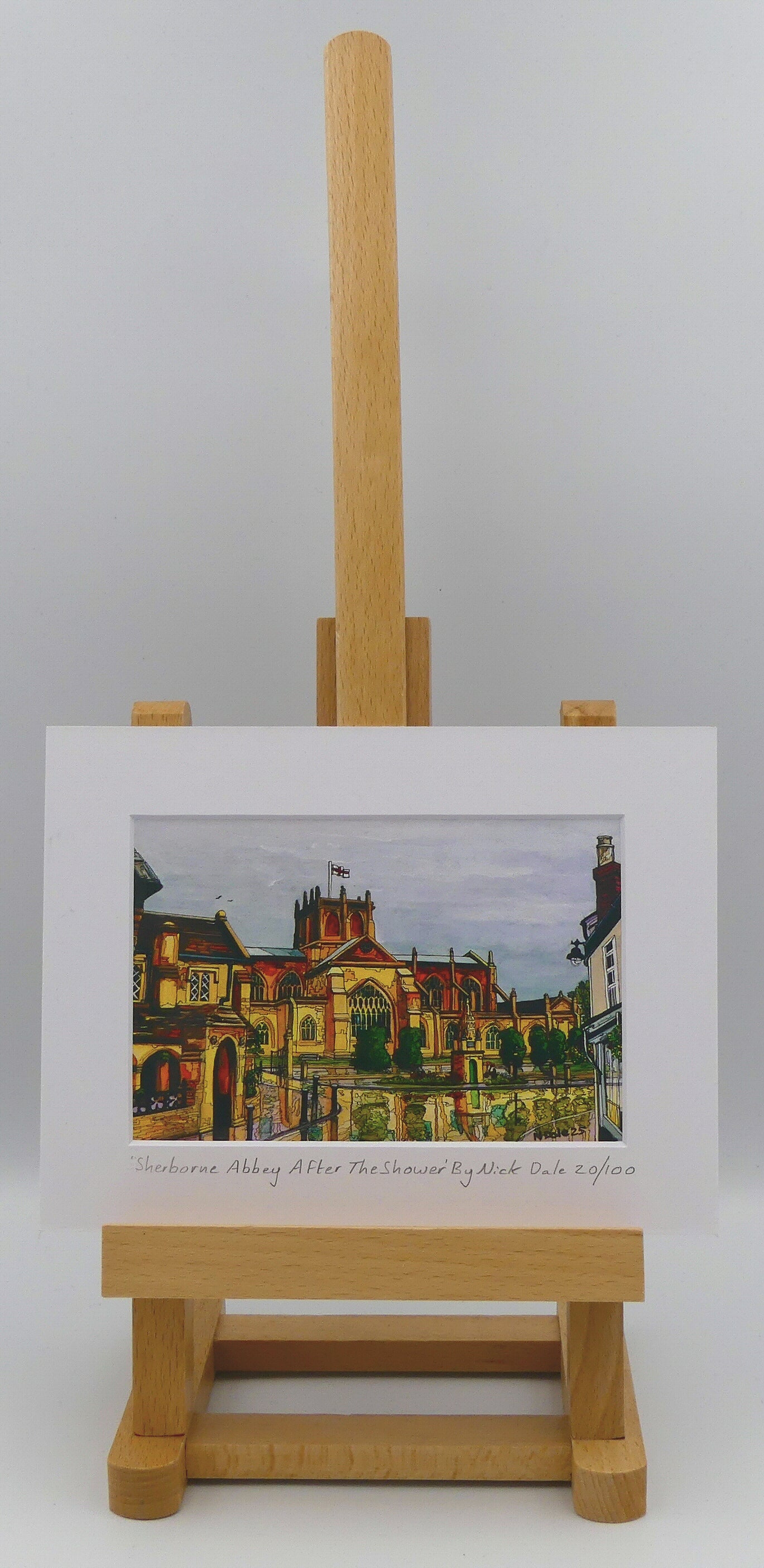 Image of Small Art Print featuring a copy of the painting 'Sherborne Abbey After The Shower' by Nick Dale. The print depicts a view of Sherborne Abbey (also known as the Abbey Church of St. Mary the Virgin), in Sherborne, Dorset. On the left hand side can be seen St Johns' Almshouse. The print is situated on a small easel.