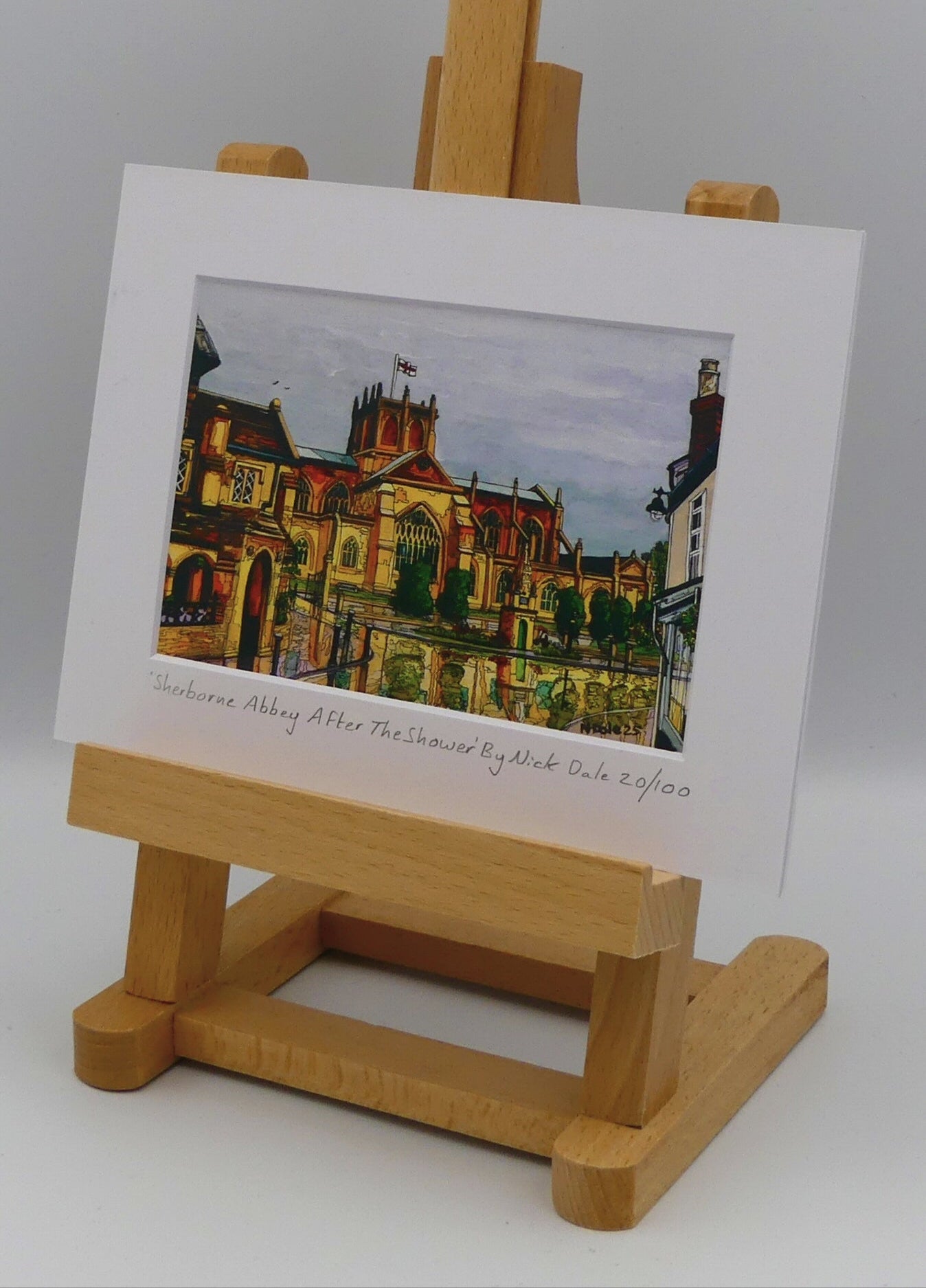 Image of Small Art Print featuring a copy of the painting 'Sherborne Abbey After The Shower' by Nick Dale. The print depicts a view of Sherborne Abbey (also known as the Abbey Church of St. Mary the Virgin), in Sherborne, Dorset. On the left hand side can be seen St Johns' Almshouse. The print is situated on a small easel.