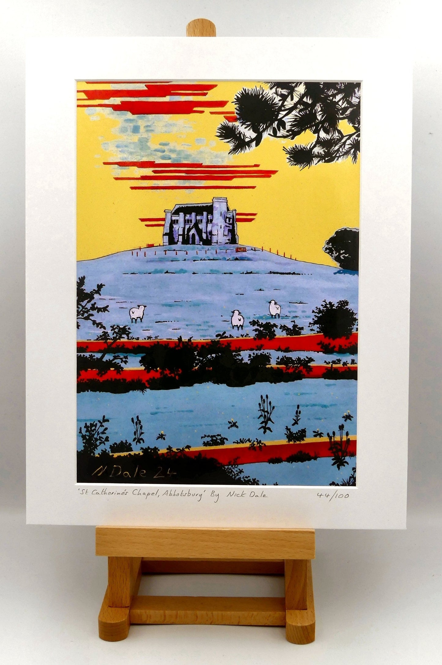 Image of a Medium Art Print (A4 size) featuring a copy of the painting 'St Catherine's Chapel, Abbotsbury' by Nick Dale. The print depicts the Medieval St Catherine's Chapel which is positioned overlooking the village of Abbotsbury. The print is situated on a small easel.