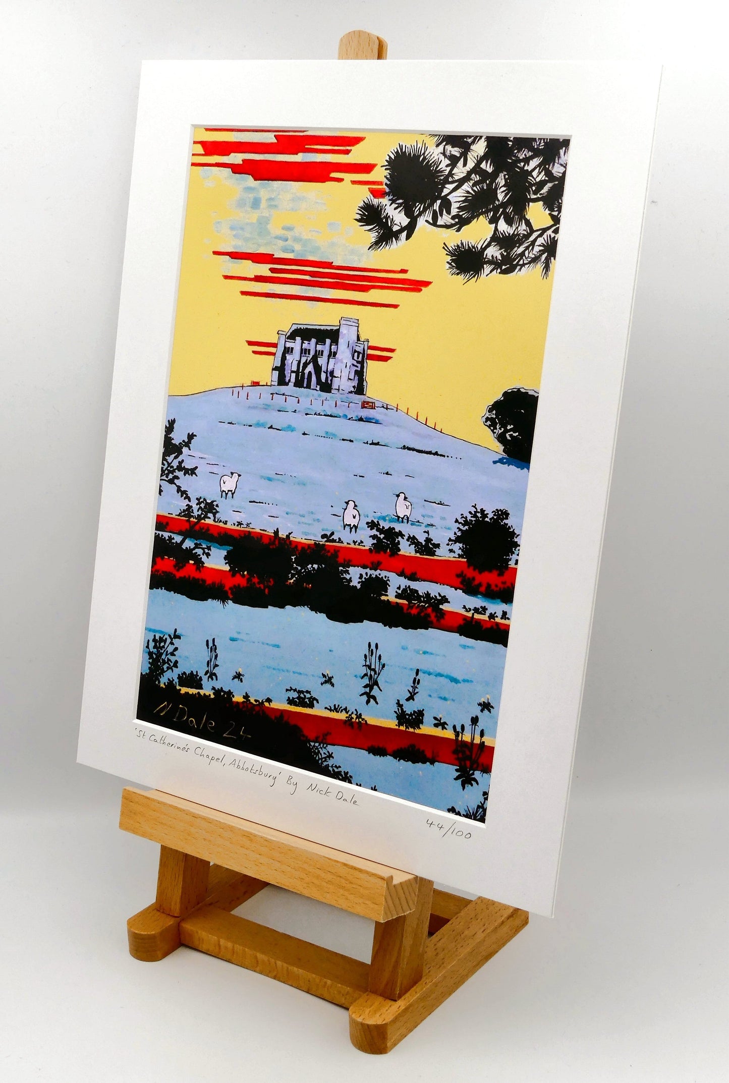 Image of a Medium Art Print (A4 size) featuring a copy of the painting 'St Catherine's Chapel, Abbotsbury' by Nick Dale. The print depicts the Medieval St Catherine's Chapel which is positioned overlooking the village of Abbotsbury. The print is situated on a small easel.