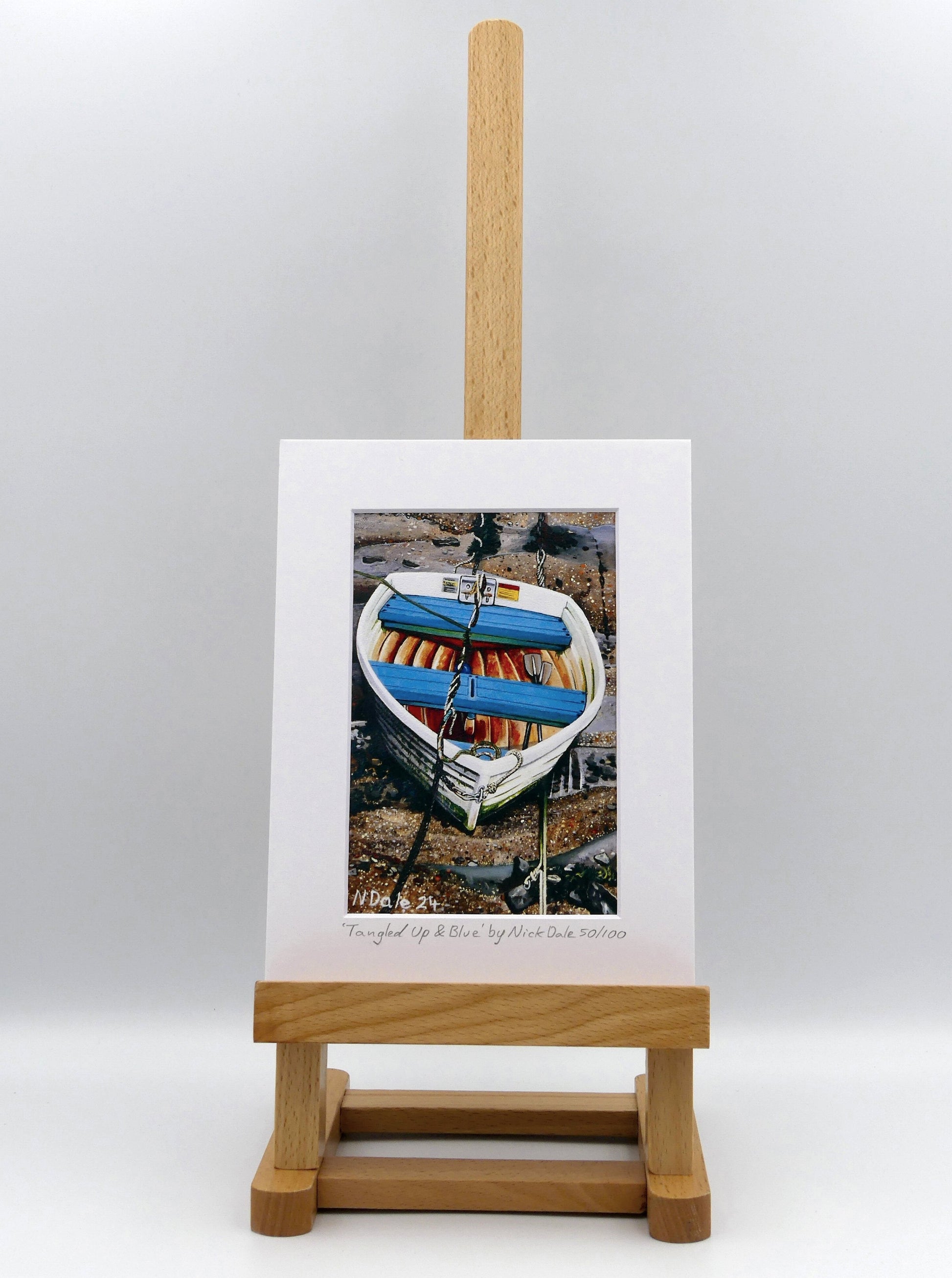 Image of a Small Art Print featuring a copy of the painting 'Tangled Up & Blue' by Nick Dale. The print depicts a small rowing boat sitting on the floor of Lynmouth Harbour at Lynmouth in Devon. The print is situated on a small easel.