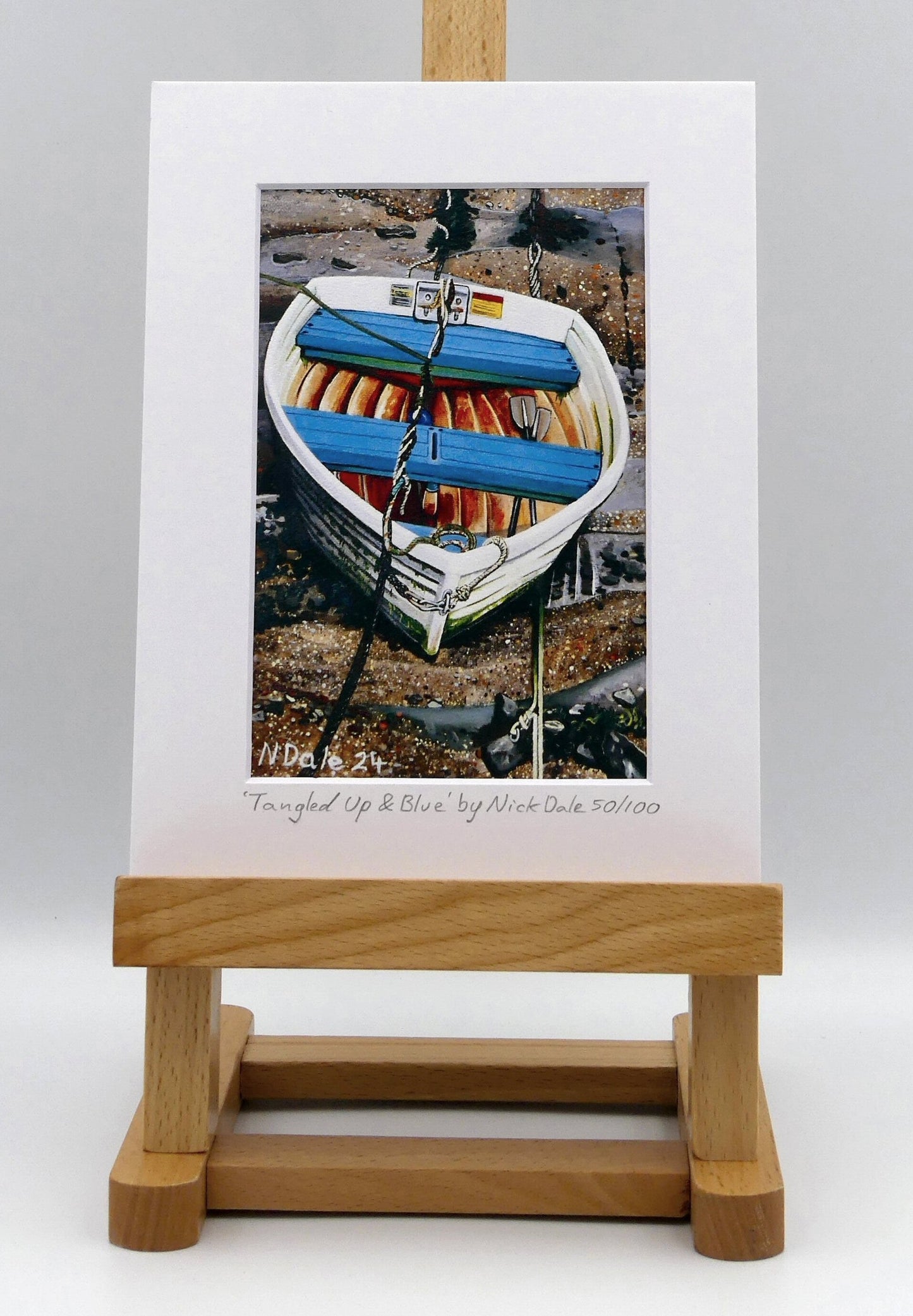 Image of a Small Art Print featuring a copy of the painting 'Tangled Up & Blue' by Nick Dale. The print depicts a small rowing boat sitting on the floor of Lynmouth Harbour at Lynmouth in Devon. The print is situated on a small easel.