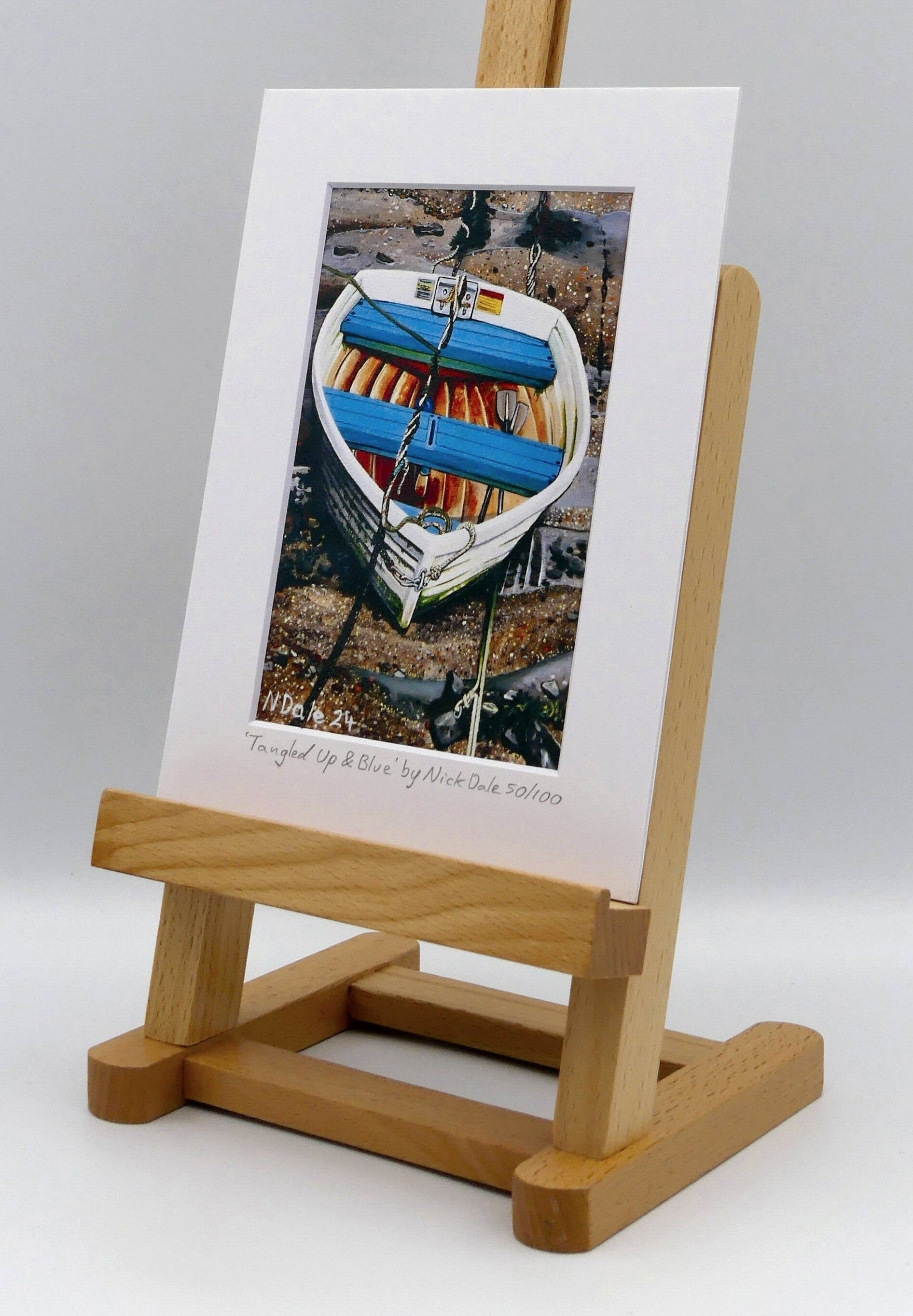 Image of a Small Art Print featuring a copy of the painting 'Tangled Up & Blue' by Nick Dale. The print depicts a small rowing boat sitting on the floor of Lynmouth Harbour at Lynmouth in Devon. The print is situated on a small easel.