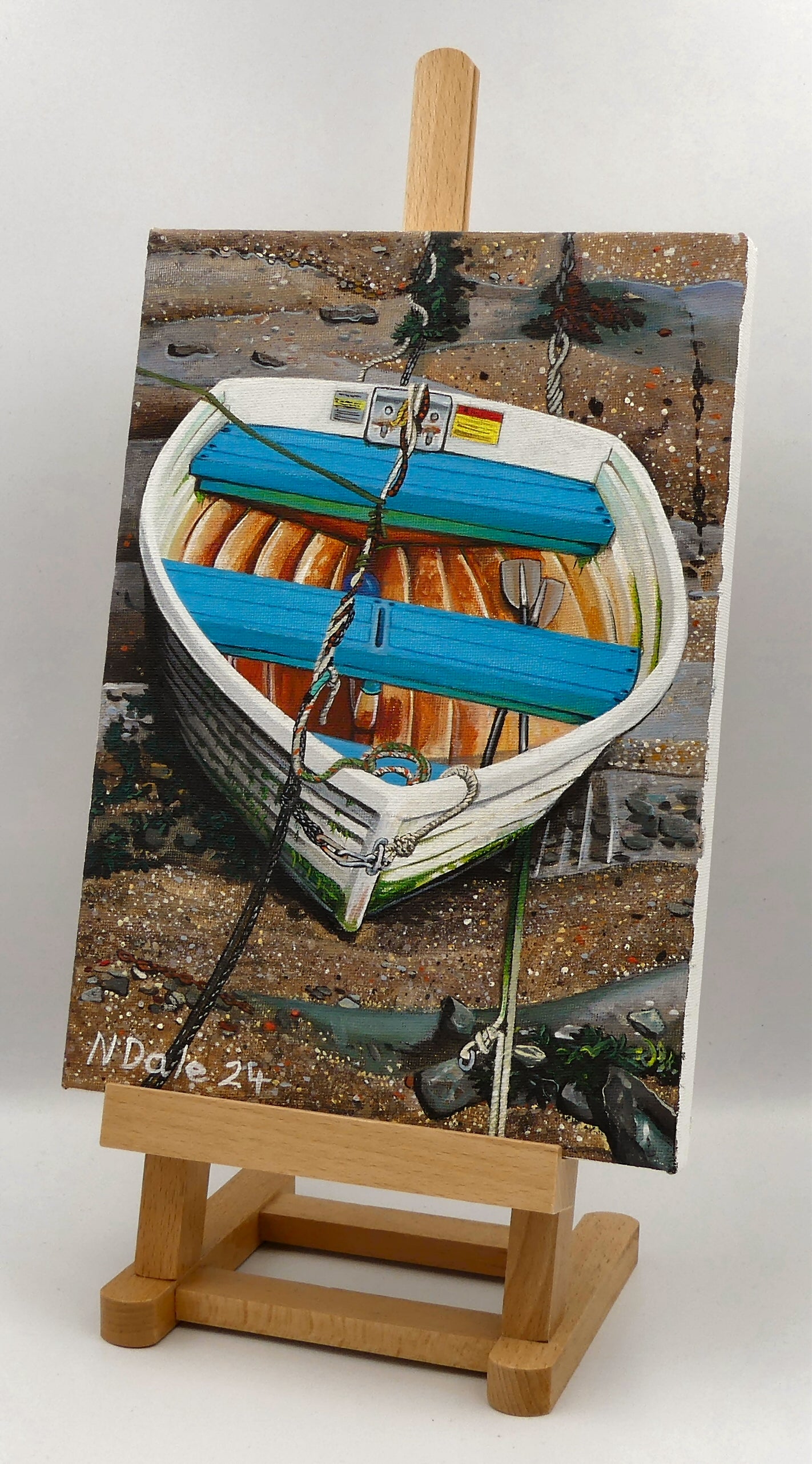 Image of the original painting 'Tangled Up & Blue' by Nick Dale on an easel. The painting depicts a small rowing boat sitting on the floor of Lynmouth Harbour at Lynmouth in Devon.