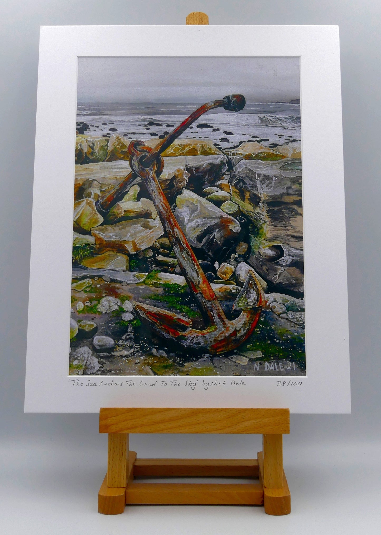 Image of a Medium Art Print featuring a copy of the painting 'The Sea Anchors The Land To The Sky' by Nick Dale. The print depicts an old anchor lying at rest under a leaden sky upon the foreshore at Chapman's Pool, near Worth Matravers, Dorset. The print is situated on a small easel.