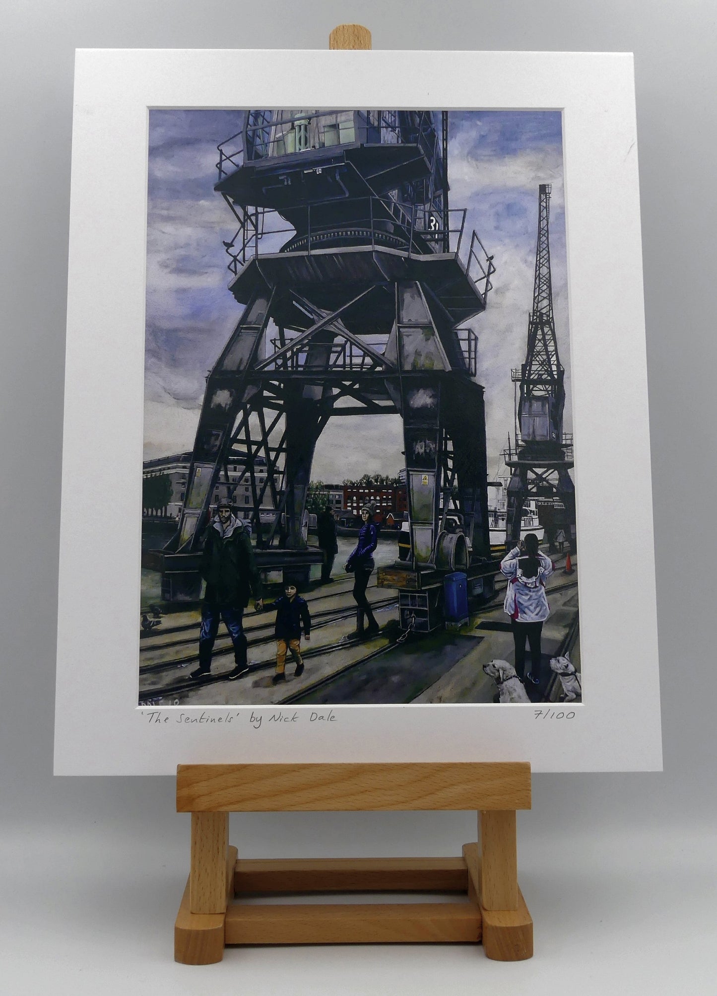 Image of a Medium Art Print featuring a copy of the painting 'The Sentinels' by Nick Dale. The print depicts the iconic tower cranes of Bristol Docks and the classic ship MV Balmoral beyond them. The print is situated on a small easel.