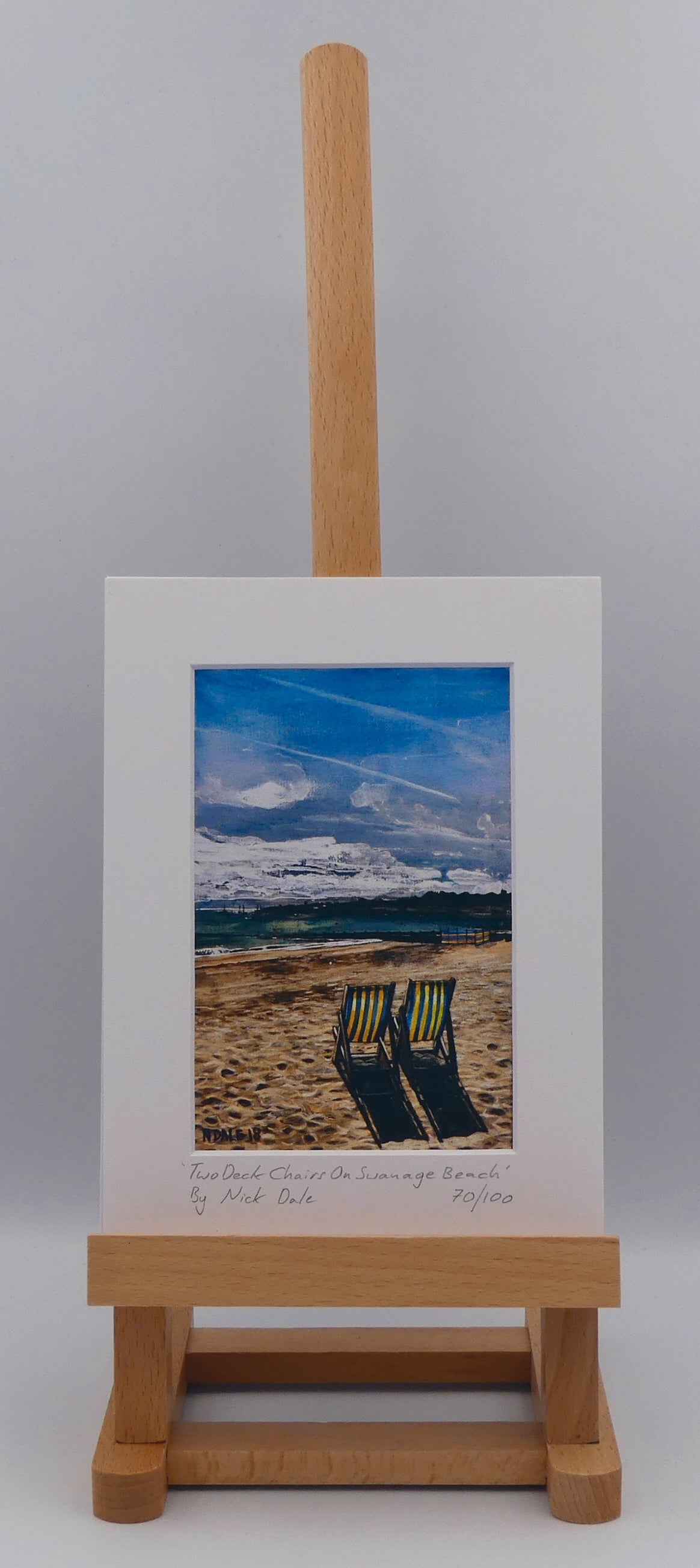 Image of a Small Art Print featuring a copy of the painting 'Two Deck Chairs On Swanage Beach' by Nick Dale. The print depicts two deck chairs overlooking the calm water from Swanage Beach (Dorset) towards Peveril Point. The print is situated on a small easel.