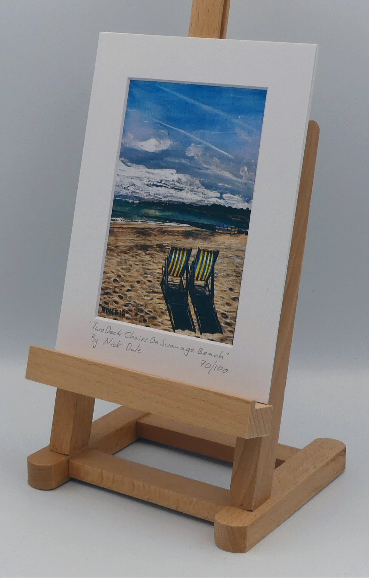 Image of a Small Art Print featuring a copy of the painting 'Two Deck Chairs On Swanage Beach' by Nick Dale. The print depicts two deck chairs overlooking the calm water from Swanage Beach (Dorset) towards Peveril Point. The print is situated on a small easel.