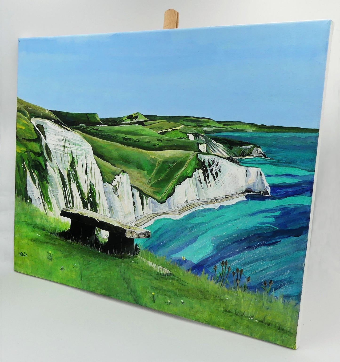 Image of the original painting 'White Nothe, SW Coast Path' by Nick Dale on a small easel. The painting depicts a view along the Jurassic Coast from the White Nothe chalk headland east of Ringstead Bay. The view looks east over Bat's Head, Swyre Head and Durdle Door to St Oswald's Bay & beyond.