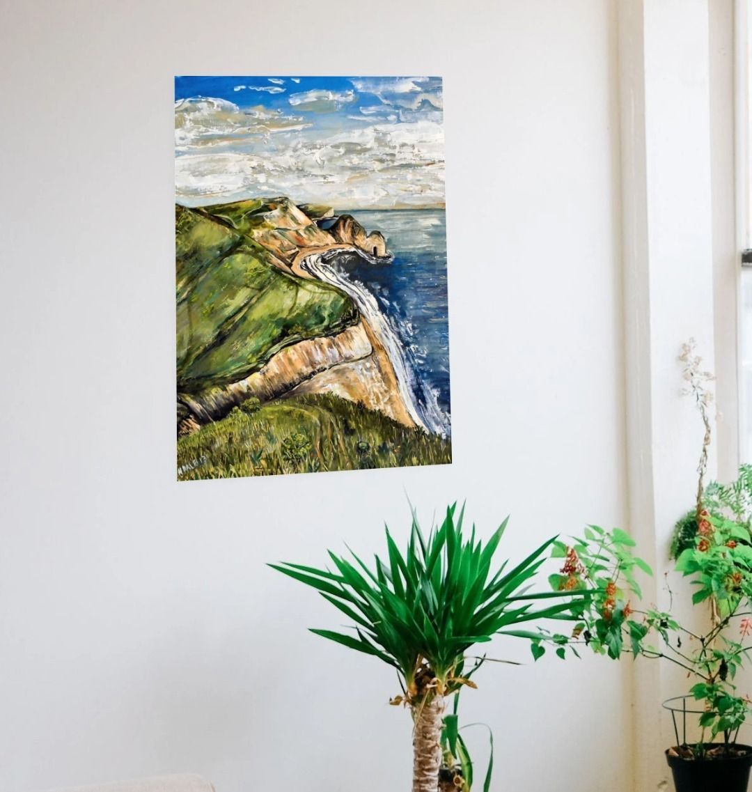 Image of a Large Art Print (A3 size) featuring a copy of the painting 'Durdle Door From The West' by Nick Dale. As displayed on a wall next to some house plants. The print depict a view along the Jurassic Coast to the famous Dorset limestone arch landmark, as seen from the coastal path to the west.