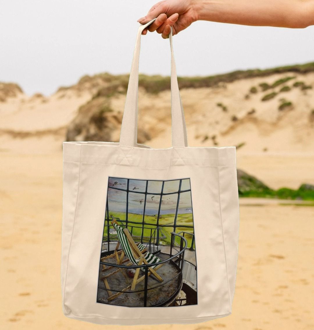 Image of a female model holding a Natural Shopper Tote Bag featuring a copy of the painting 'Let's Be Together Alone' by Nick Dale. The bag depicts the view from the lantern room of the Old Light lighthouse on Beacon Hill, on the island of Lundy, Devon.