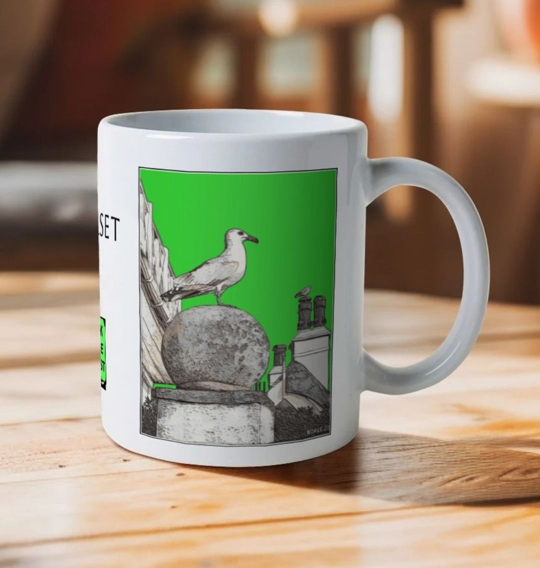 Image of a White Mug on a wooden table featuring a modified copy of the painting 'A View Of The Sea At Lyme Regis' by Nick Dale - this being the 'Green' version. The handle is orientated to the right. The mug depicts a gull and buildings along Marine Parade, Lyme Regis.