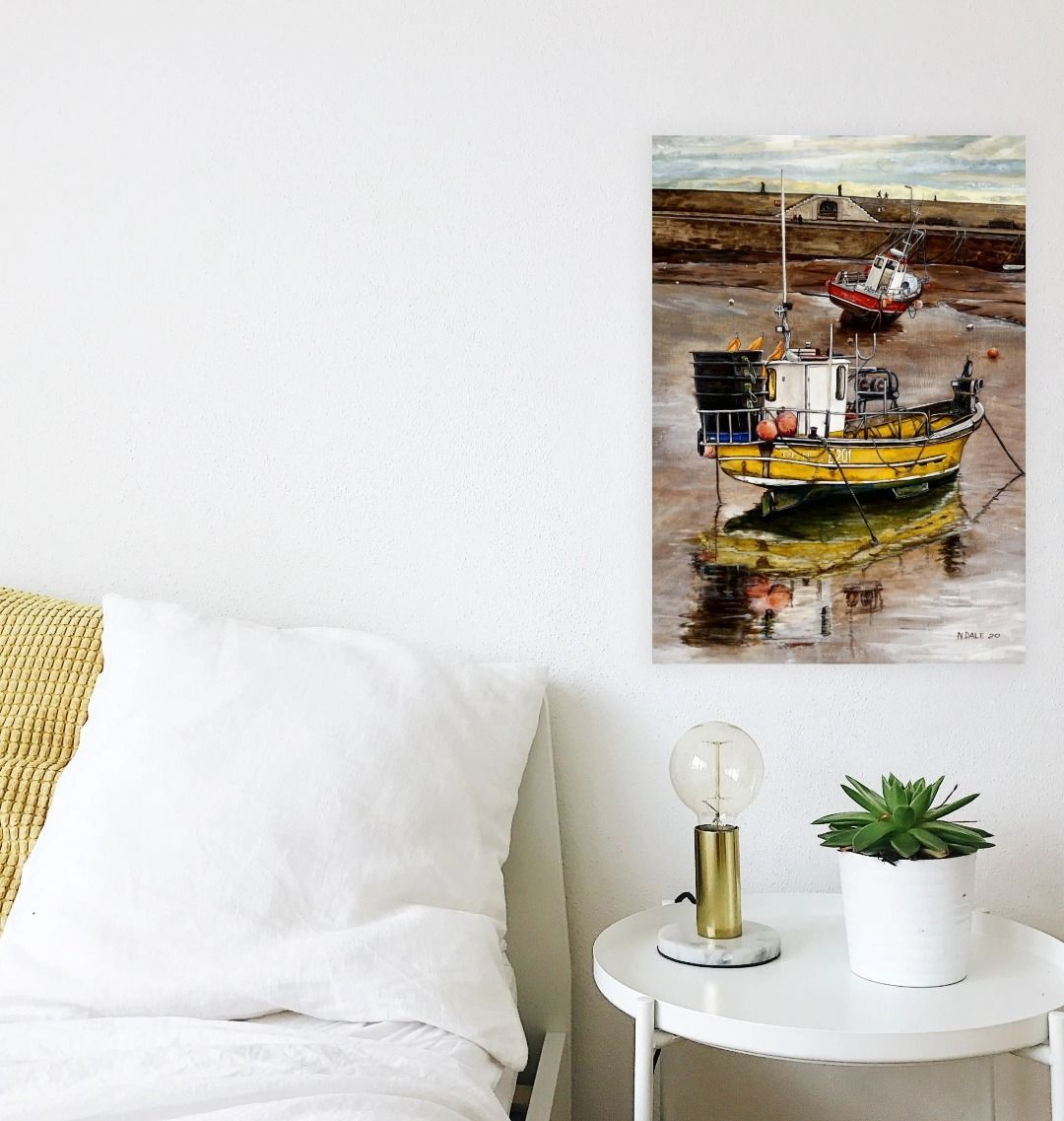 Image of a Large Art Print (A3 size) featuring a copy of the painting 'Lyme Regis at Low Tide' by Nick Dale. As displayed on a wall next to a bed. The print depicts a sunset where the fishing vessels rest on the floor of Lyme Regis harbour whilst the tourists enjoy the view from the Cobb.
