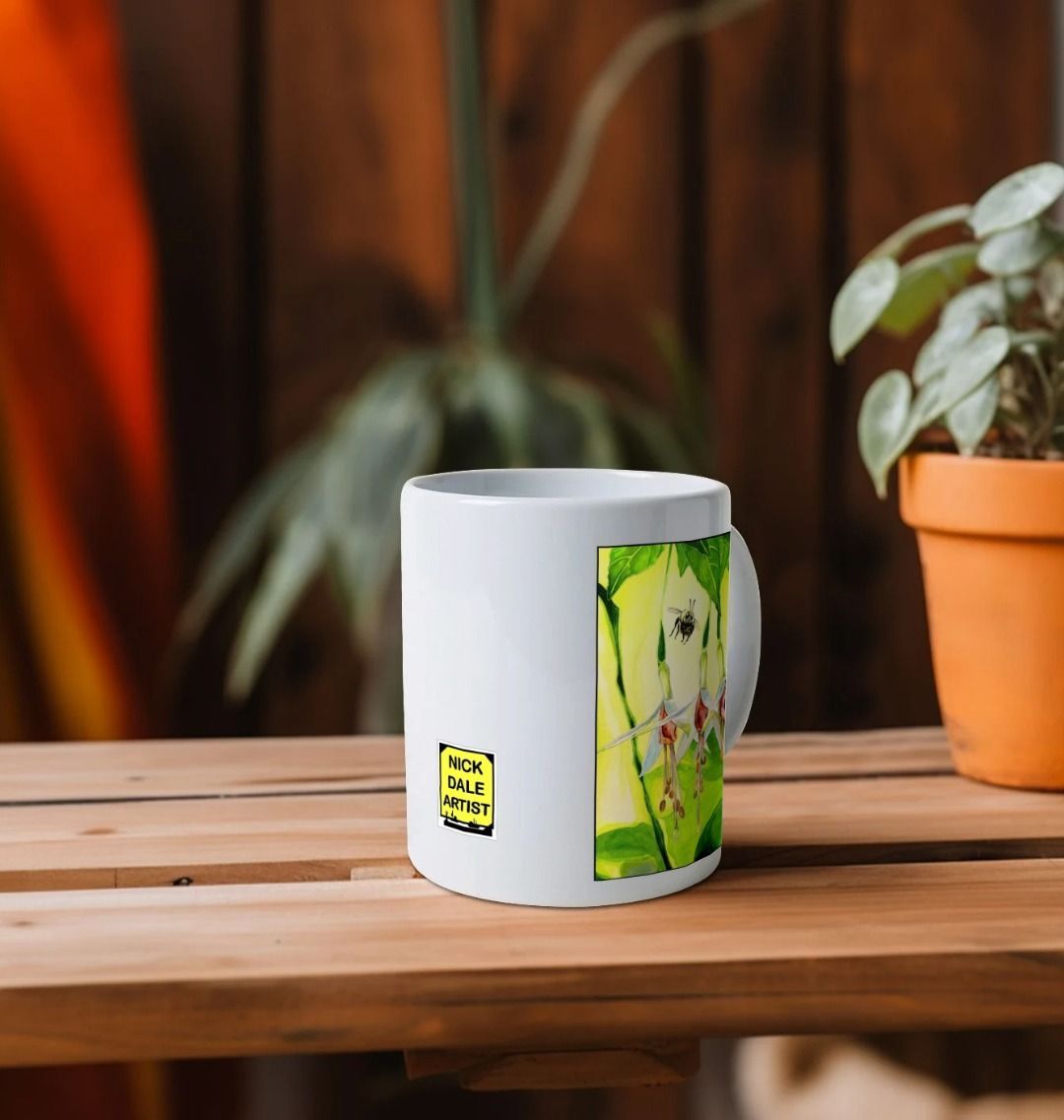 Image of a White Mug on a wooden shelf featuring a copy of the painting 'The Three Muses' by Nick Dale. Image also shows the artist's logo on the mug. The mug handle is obscured behind the mug. The mug depicts a close-up view of a bee approaching its prize. But which will it choose?