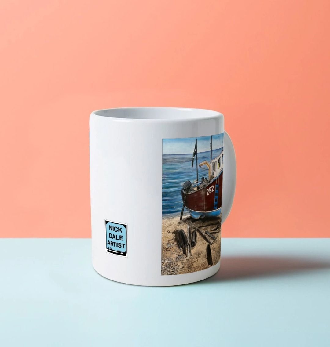 Image of a White Mug on a blue worksurface featuring a copy of the painting 'Relaxing Beer' by Nick Dale. Image also shows the artist's logo on the mug. The mug handle is obscured behind the mug. The mug depicts a fishing boat beached at Beer, Devon. The wood is laid under the boats to aid in their winching up the shingle beach.