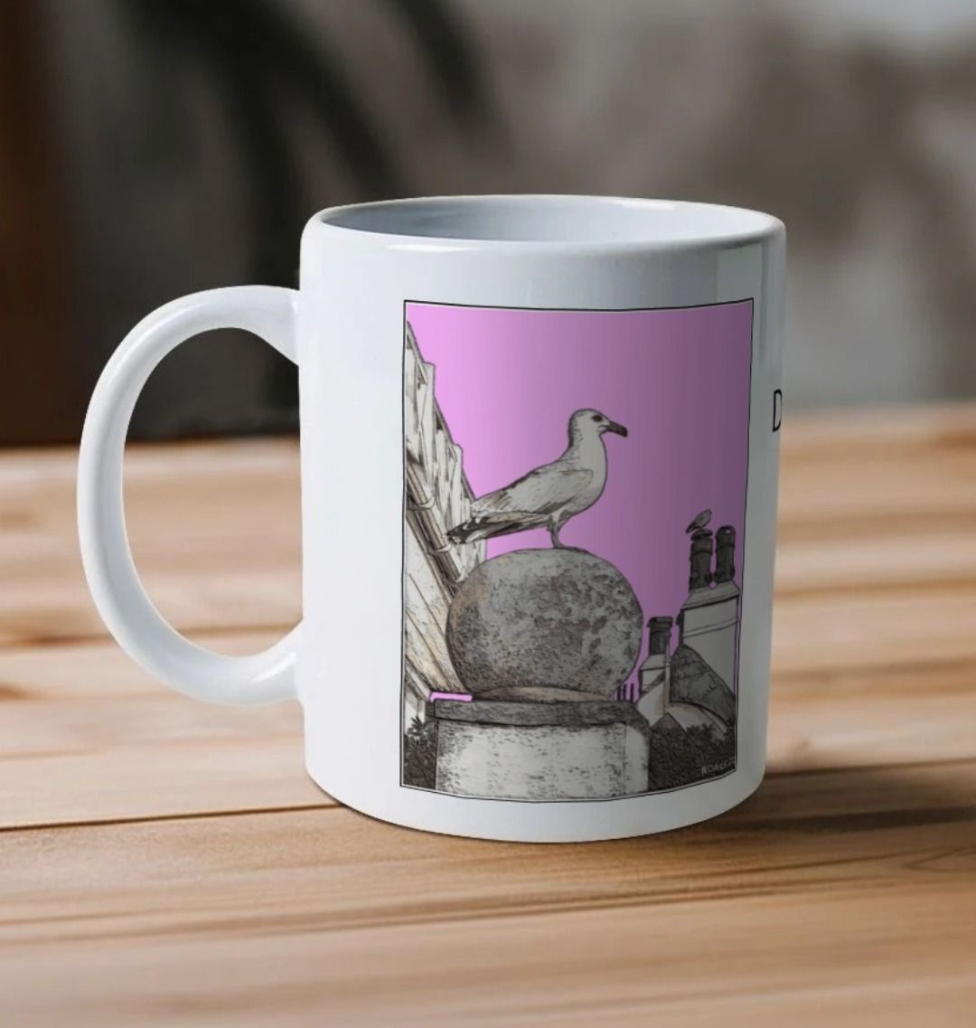 Image of a White Mug on a wooden table featuring a modified copy of the painting 'A View Of The Sea At Lyme Regis' by Nick Dale - this being the 'Pink' version. The handle is orientated to the left. The mug depicts a gull and buildings along Marine Parade, Lyme Regis.